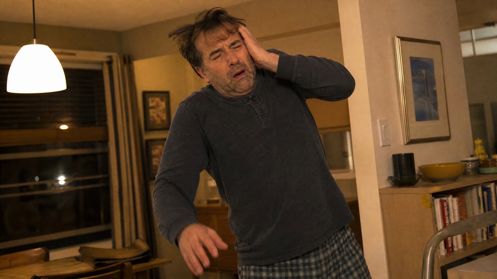 A man mid-motion gripping the side of his head with a sudden, startled expression, illustrating the abrupt onset of a thunderclap headache