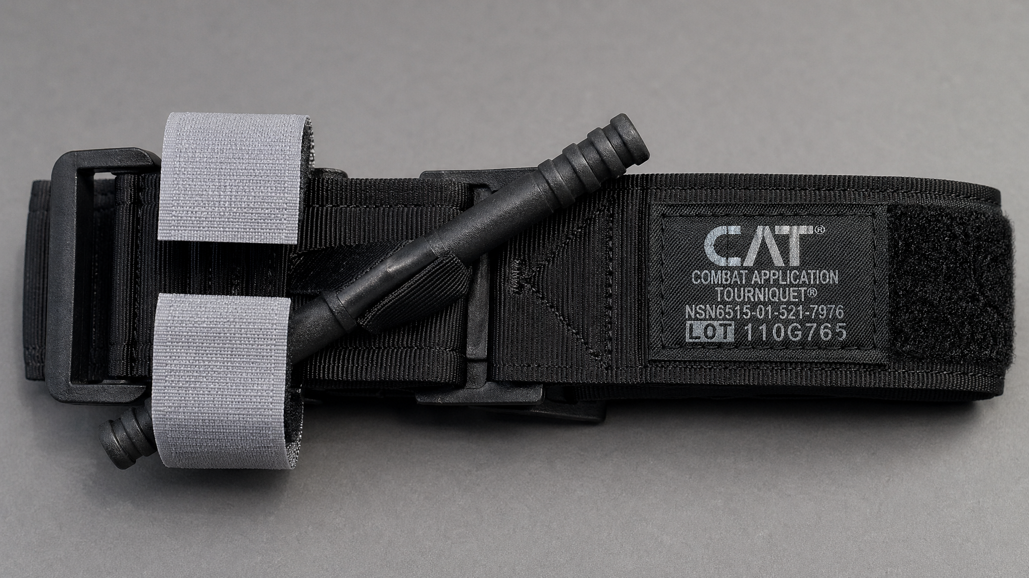 Close-up of a CAT tourniquet band and windlass rod on a neutral surface, product detail shot, clean lighting