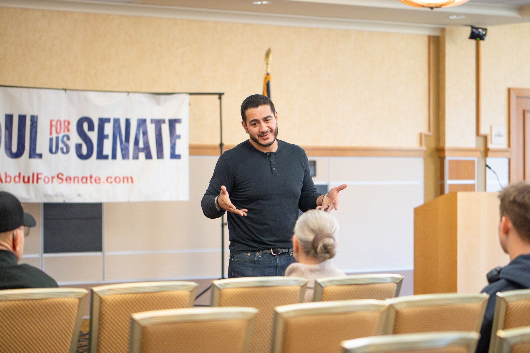 Abdul El-Sayed speaking at a campaign event in front of a banner reading Abdul For US Senate