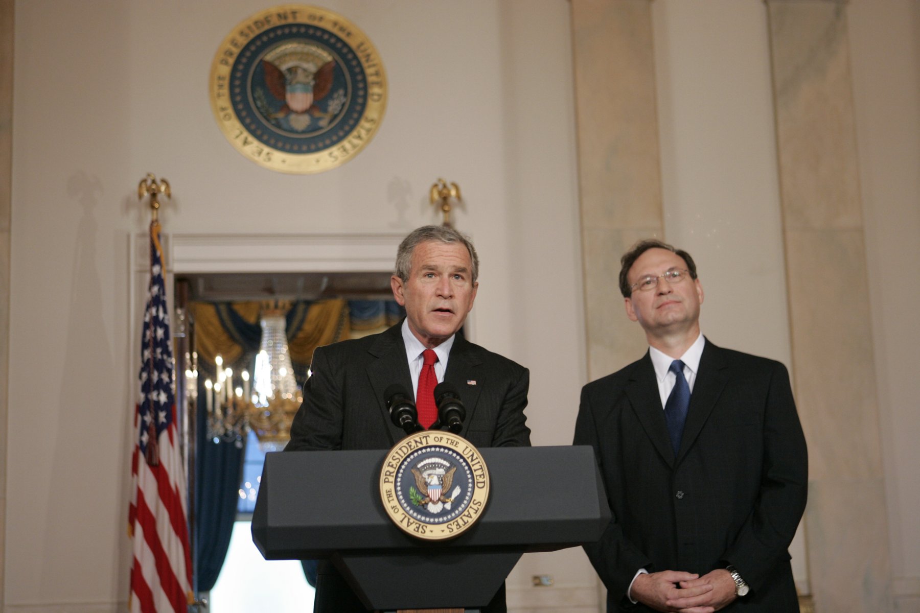 President George W. Bush at a podium announcing the nomination of Samuel Alito, who stands beside him, in the White House Cross Hall on Oct. 31, 2005