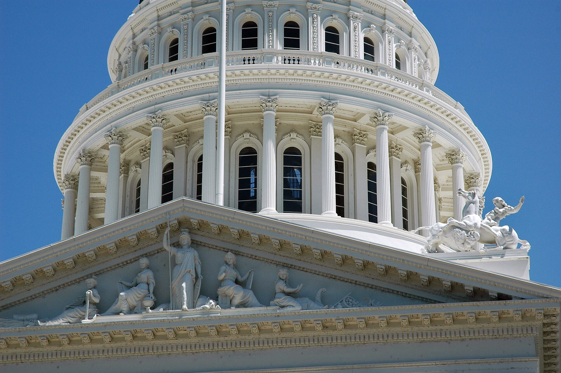 Dome and pediment sculptures of the California State Capitol in Sacramento against a blue sky