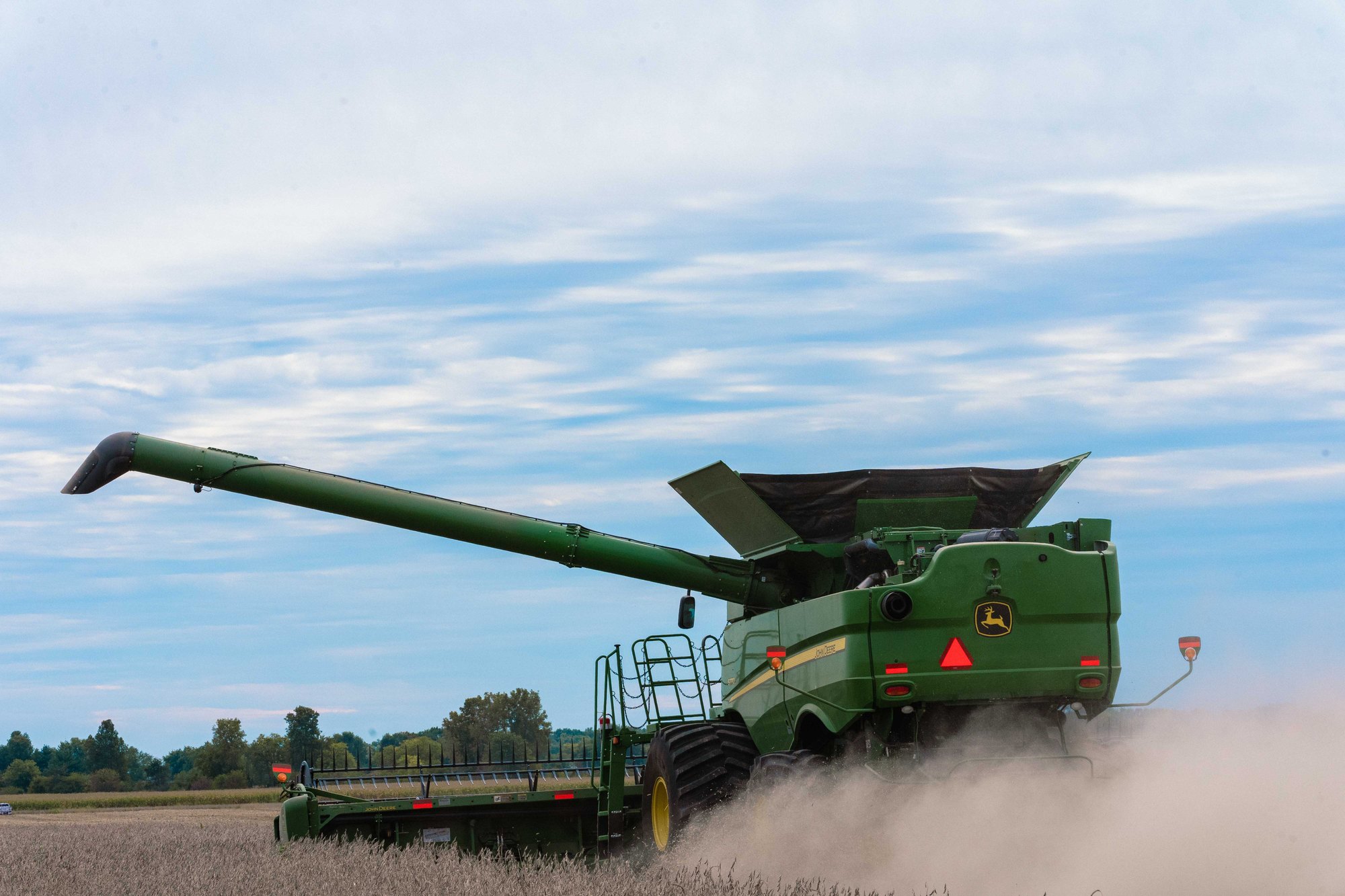 A green John Deere combine harvesting soybeans in a field in Brownsburg, Indiana, kicking up dust