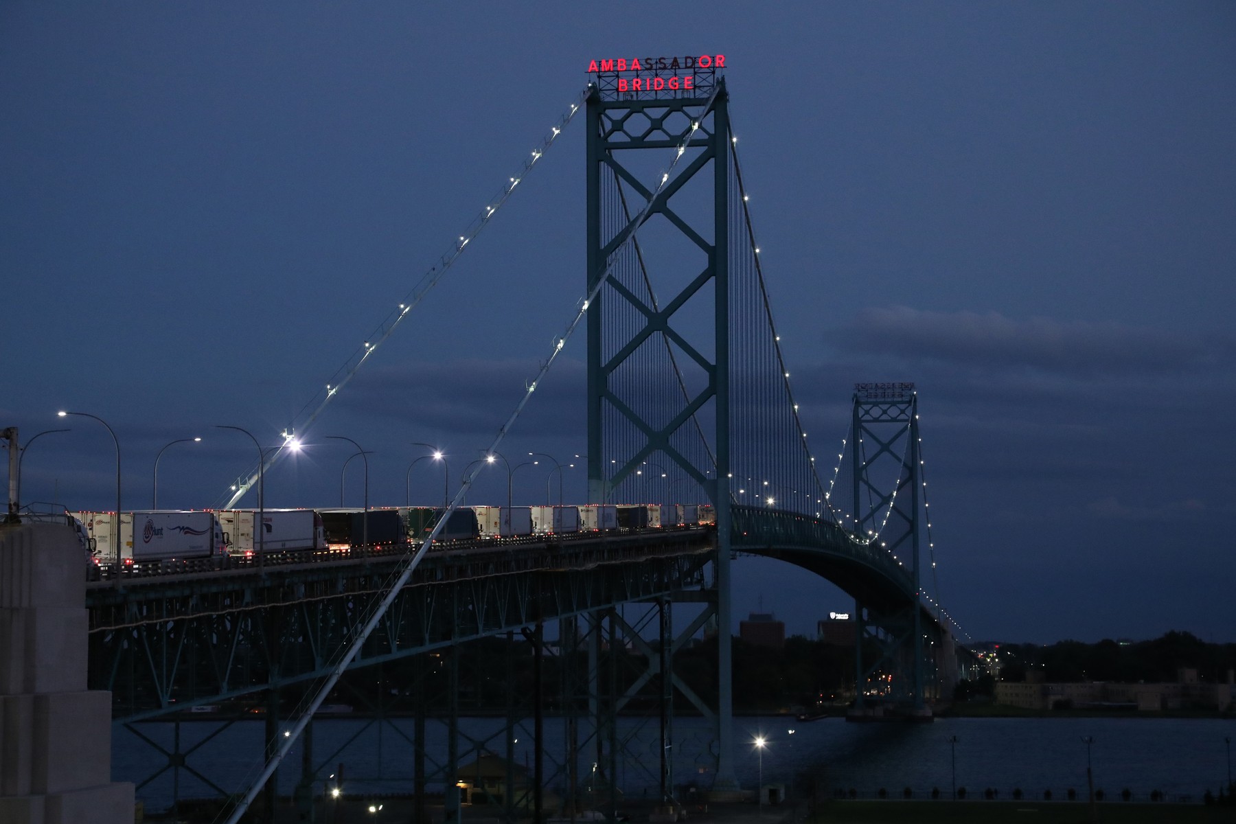 Freight trucks lined up at dusk on the Ambassador Bridge connecting Detroit, Michigan and Windsor, Ontario