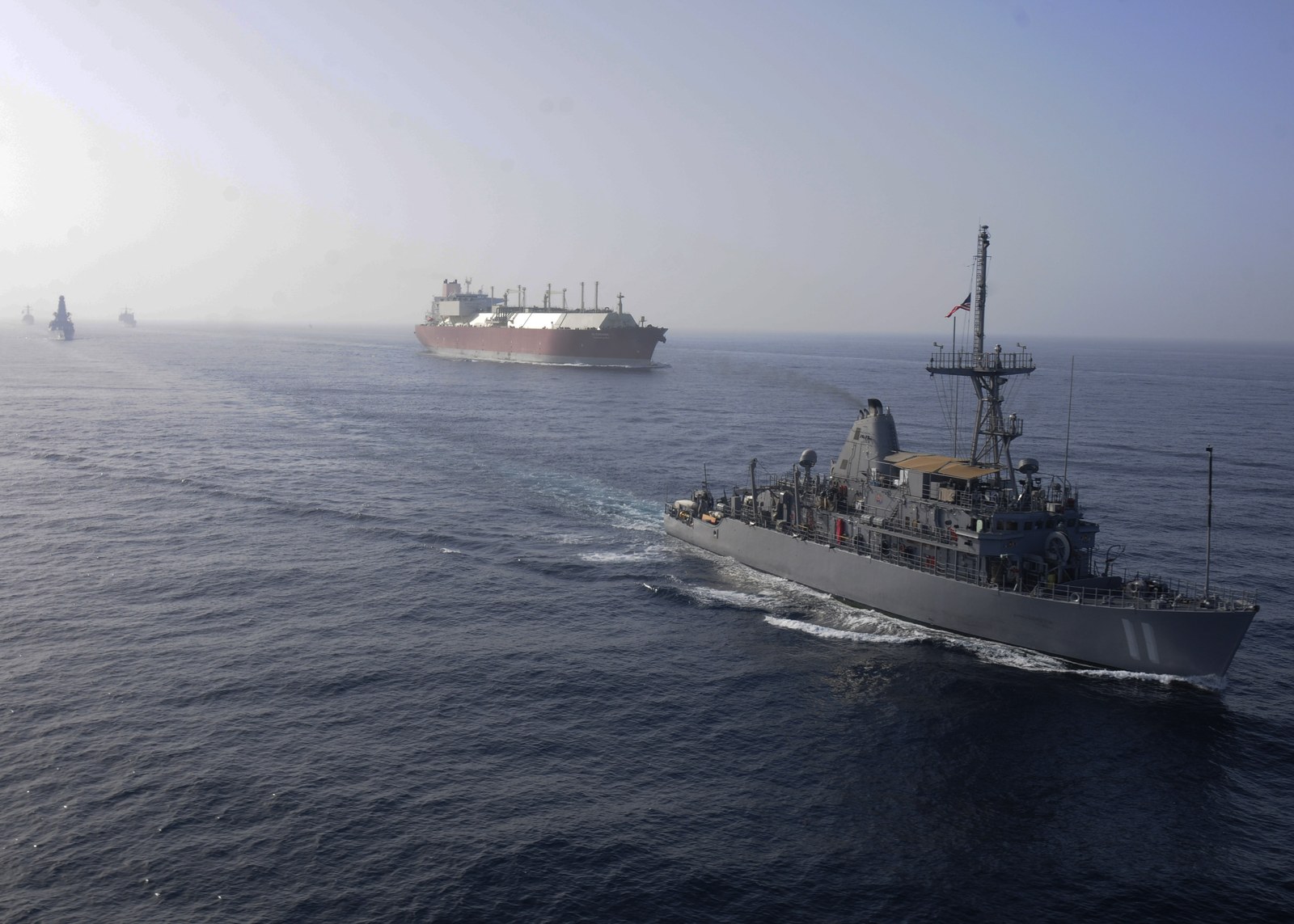 A U.S. Navy mine countermeasures ship escorting a large liquefied natural gas tanker in the Persian Gulf