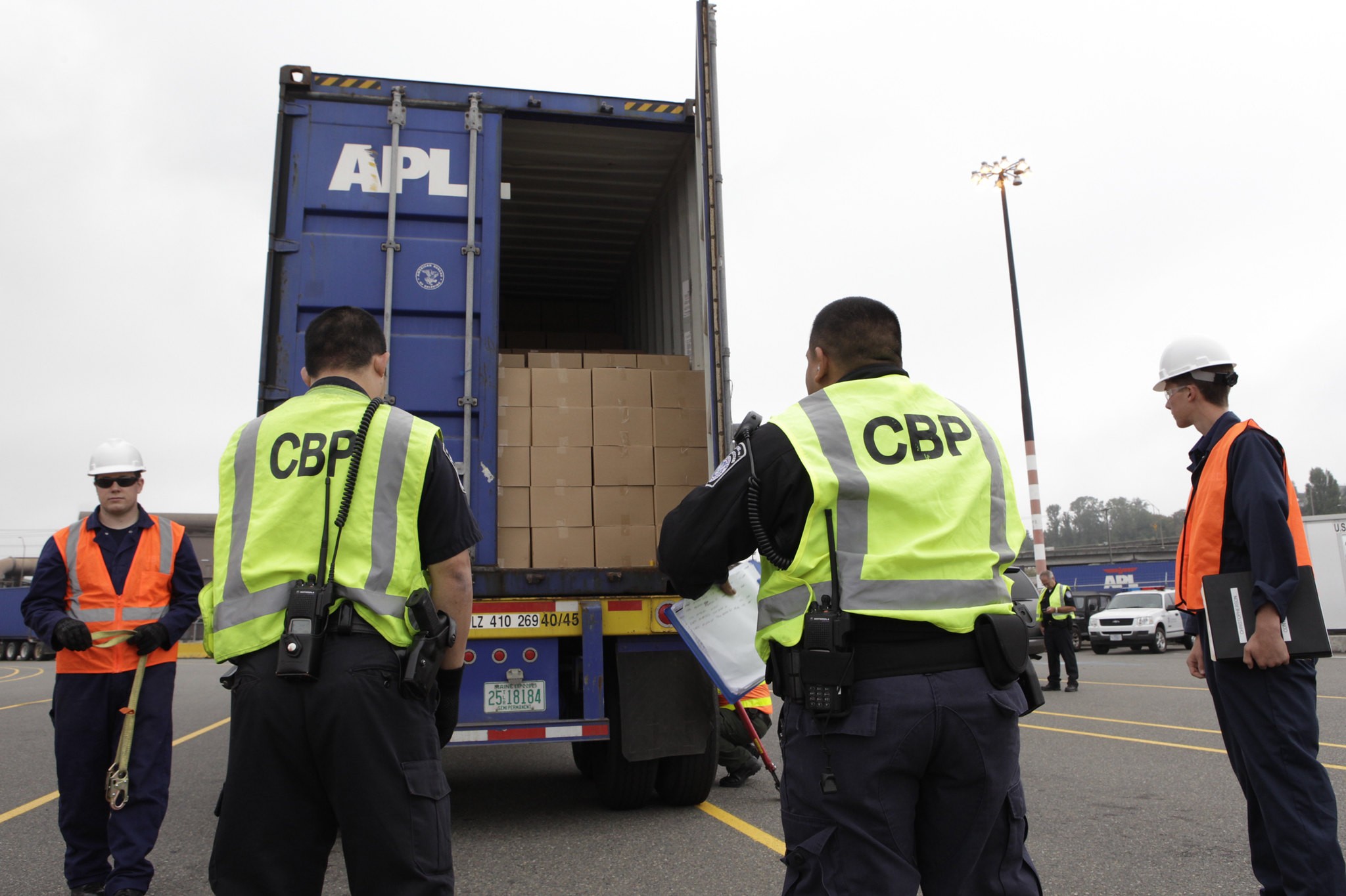 Two U.S. Customs and Border Protection officers in CBP safety vests inspect a shipping container at a Seattle port of entry