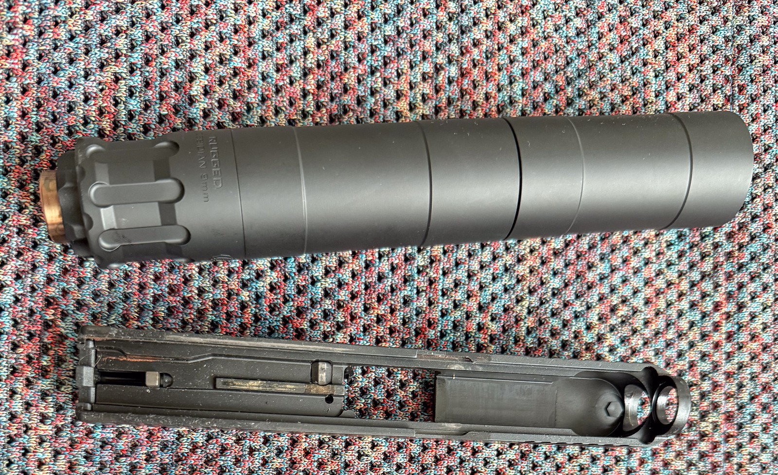 A Rugged Obsidian 9mm suppressor next to a disassembled Glock pistol slide and threaded barrel