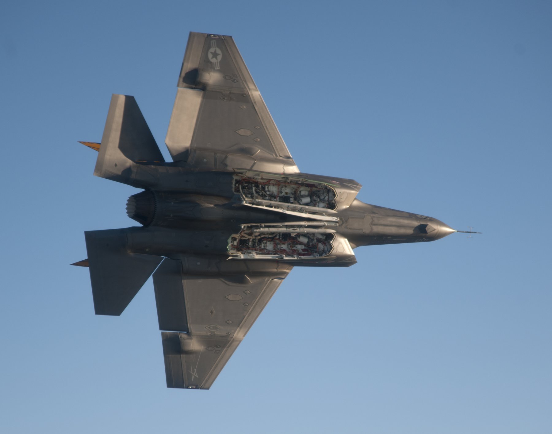 An F-35C Lightning II in flight with its internal weapons bay doors open, showing AIM-120 missiles inside