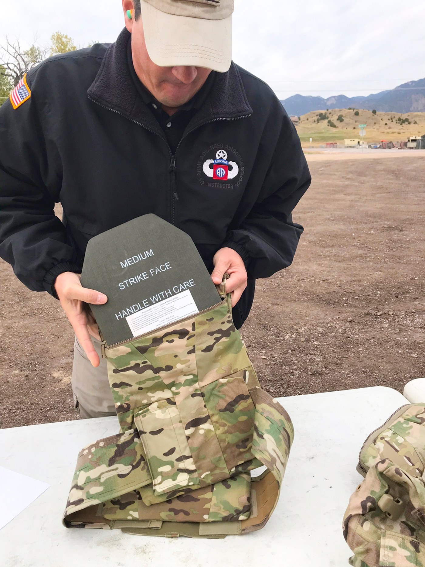 A trainer slides a ballistic plate marked Medium Strike Face into the plate carrier of a modular scalable vest