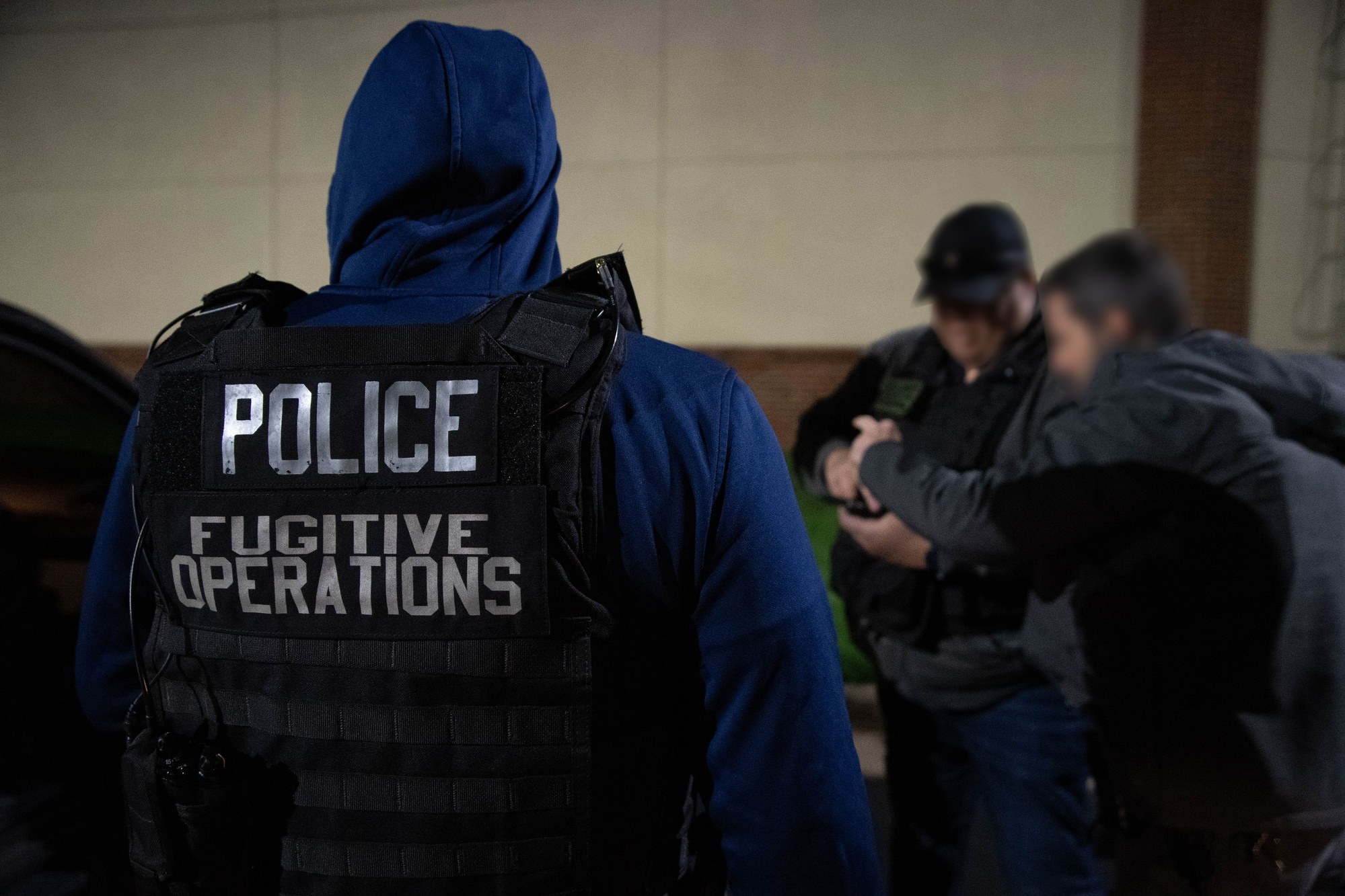 ICE Enforcement and Removal Operations officer in a Police Fugitive Operations vest during an arrest at night