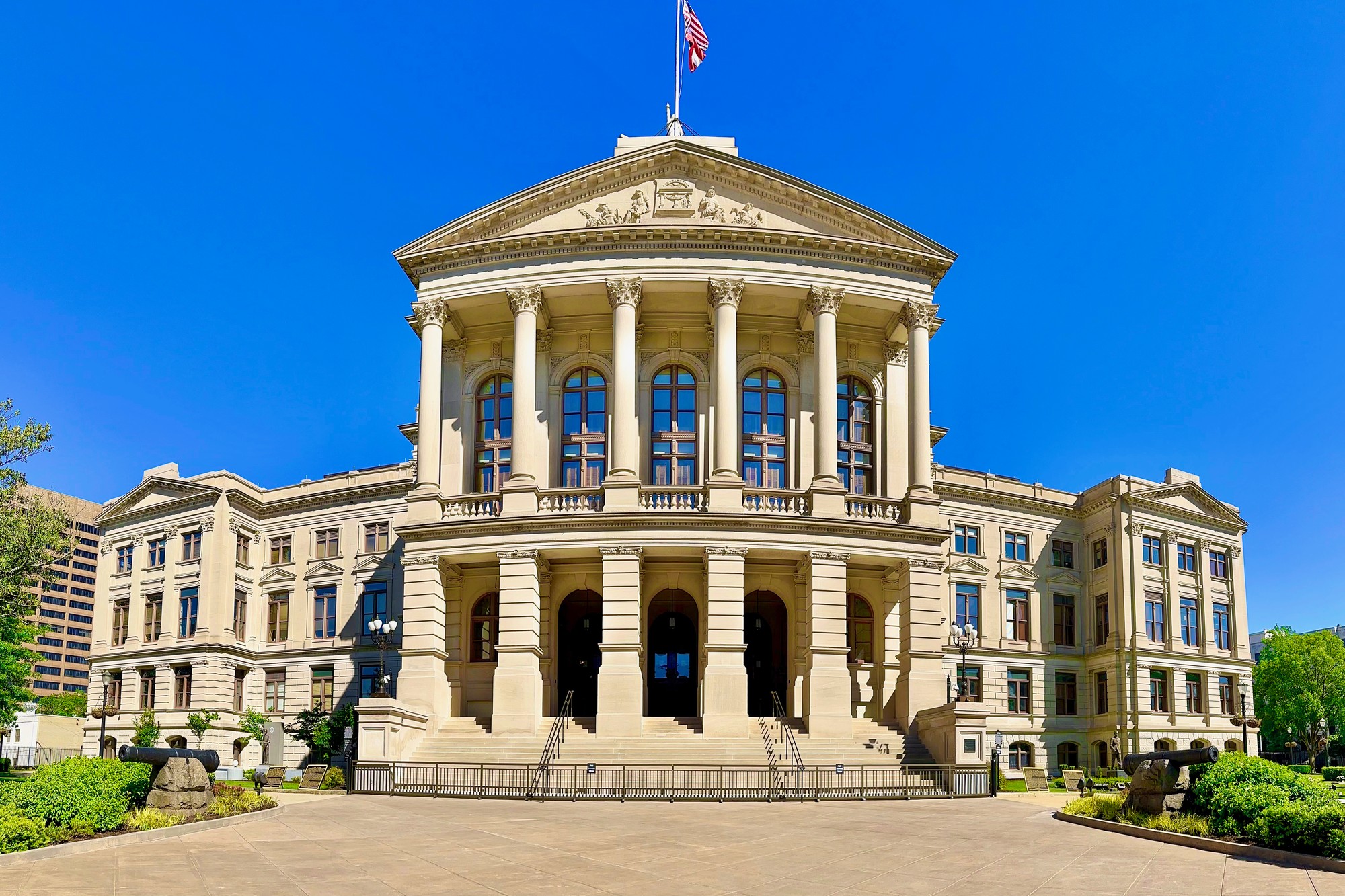 The west front of the Georgia State Capitol in Atlanta, with the American flag flying above the pediment and Civil War cannons on the lawn