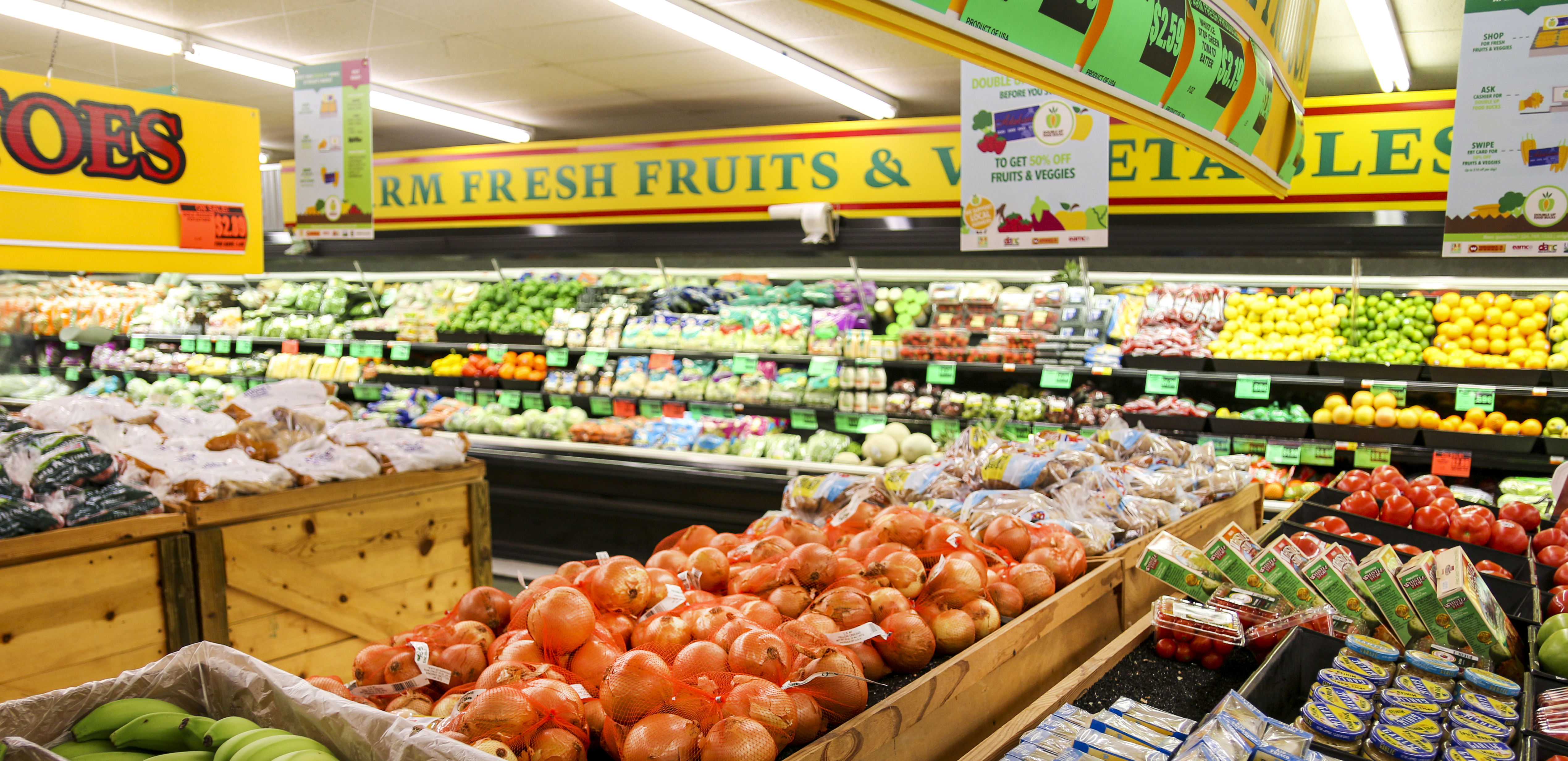 Produce aisle in a grocery store with price signage over fresh fruits and vegetables
