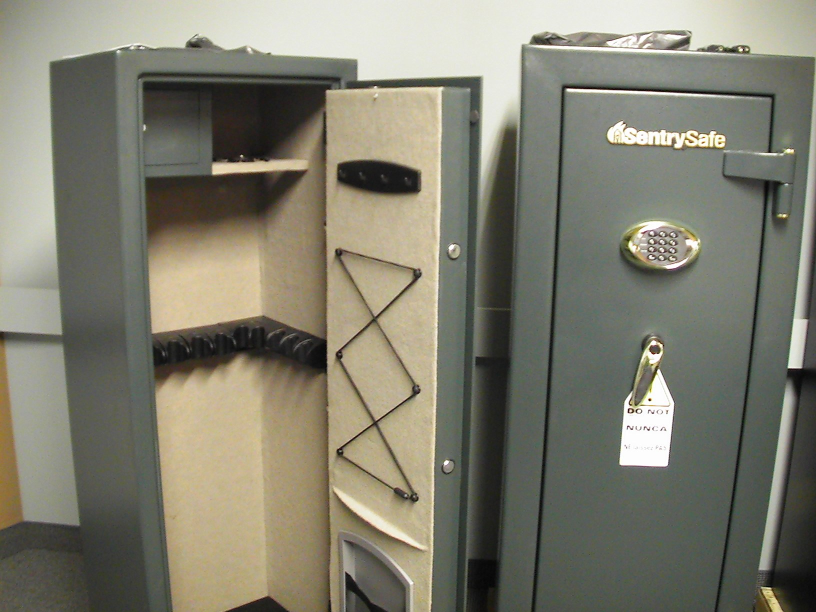 Two gray SentrySafe gun safes, one open showing a carpeted rack interior and one closed with an electronic keypad