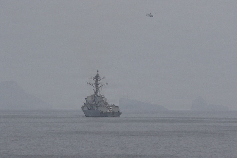 A U.S. Navy guided-missile destroyer operating in the Strait of Hormuz with a helicopter overhead during mine clearance operations