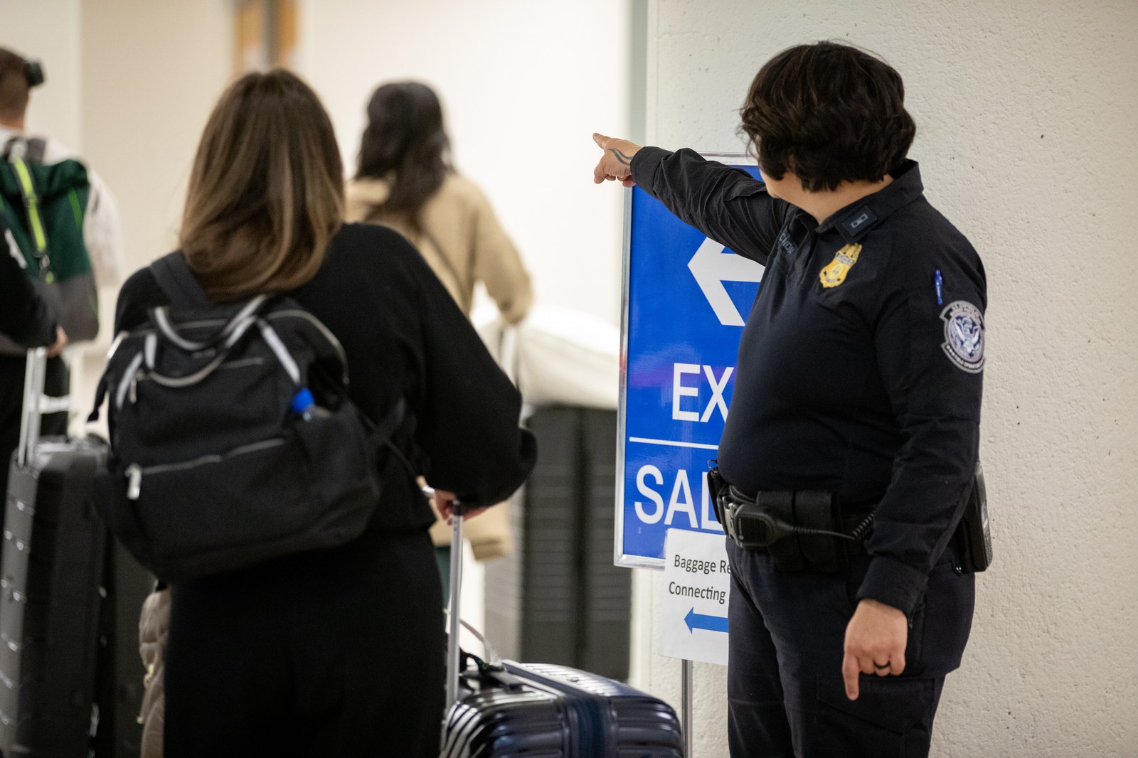 A U.S. Customs and Border Protection officer directs arriving international passengers toward the exit in the baggage claim area at Phoenix Sky Harbor International Airport