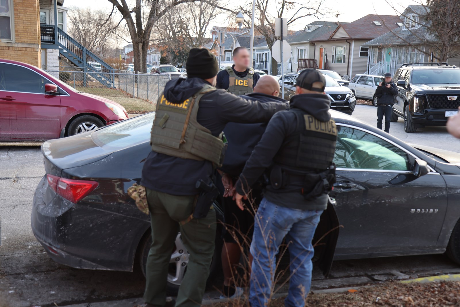 ICE Enforcement and Removal Operations officers and police take a man into custody beside a car on a Chicago street