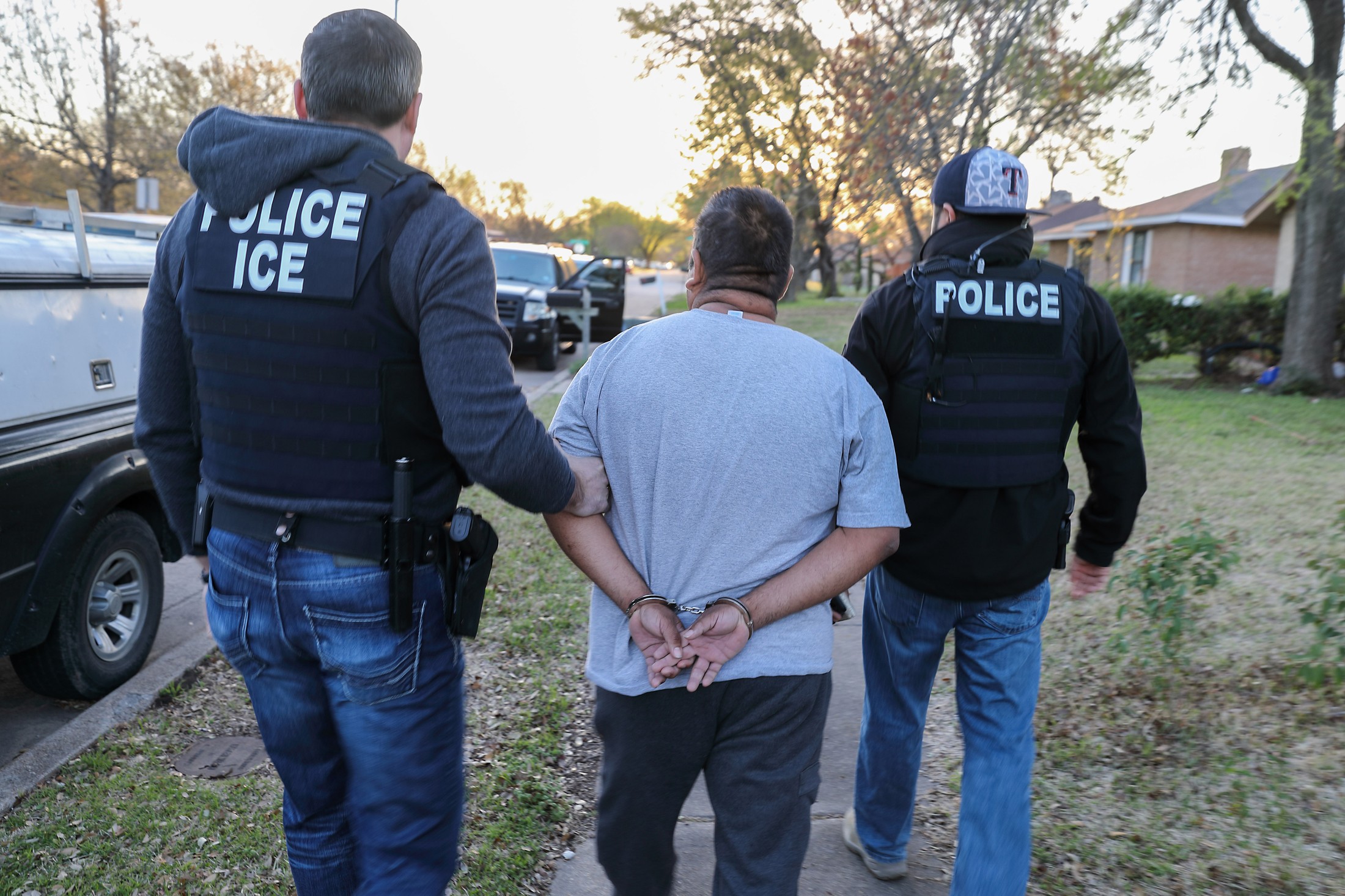 ICE Enforcement and Removal Operations officers escort a handcuffed man during a targeted enforcement operation
