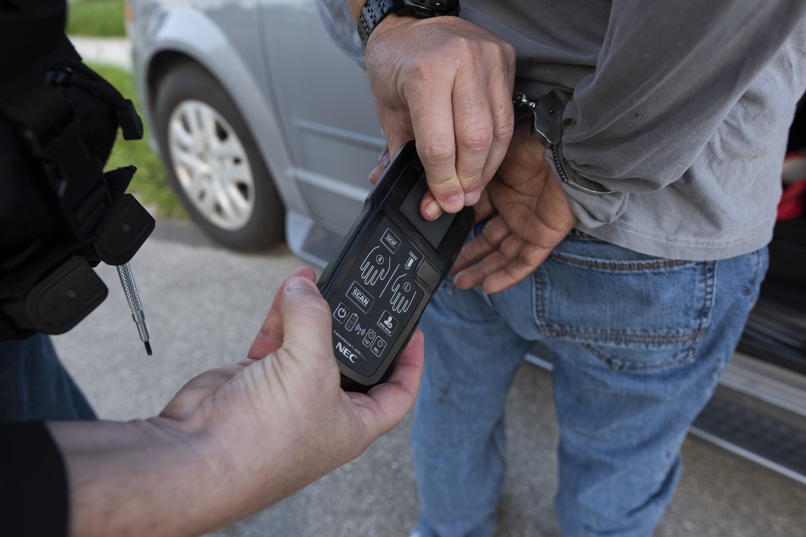 An ICE officer runs a handheld biometric identification device on a handcuffed man during a targeted enforcement operation in Florida