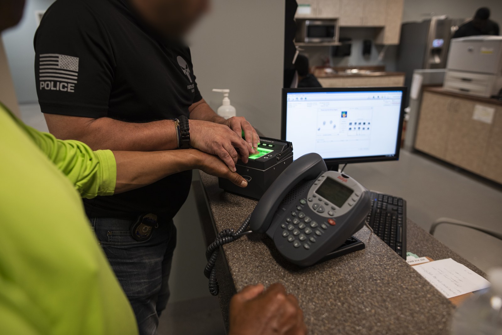 An ICE Enforcement and Removal Operations officer runs an arrestee's fingerprints at a processing station, with the biometric record open on the computer screen