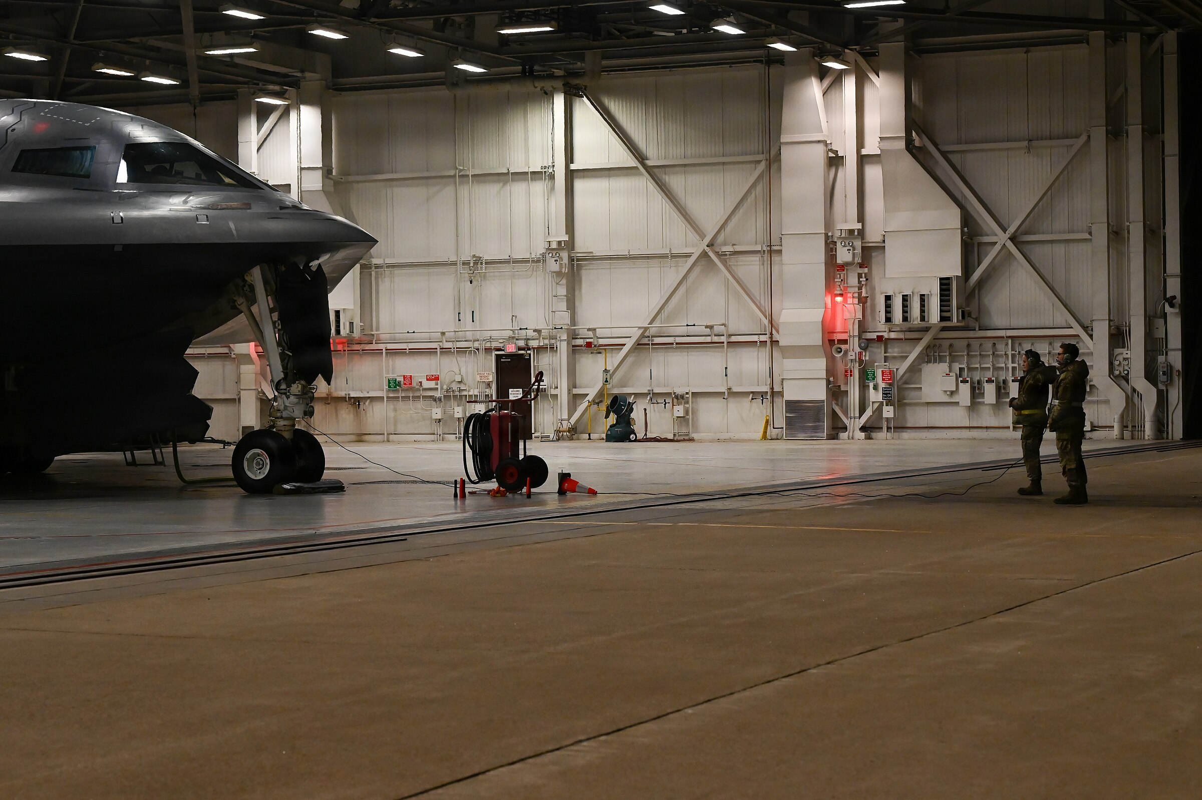 B-2 Spirit nose and landing gear in a hangar with two airmen standing nearby