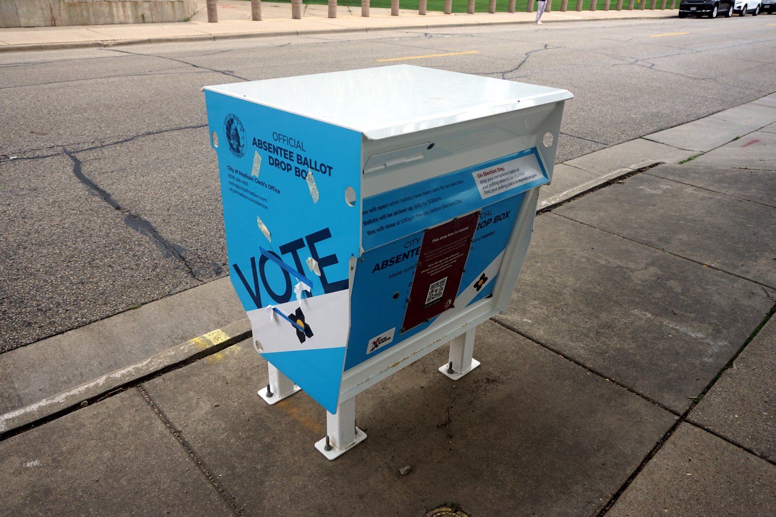 An official City of Madison, Wisconsin absentee ballot drop box on a sidewalk, its ballot slot taped shut