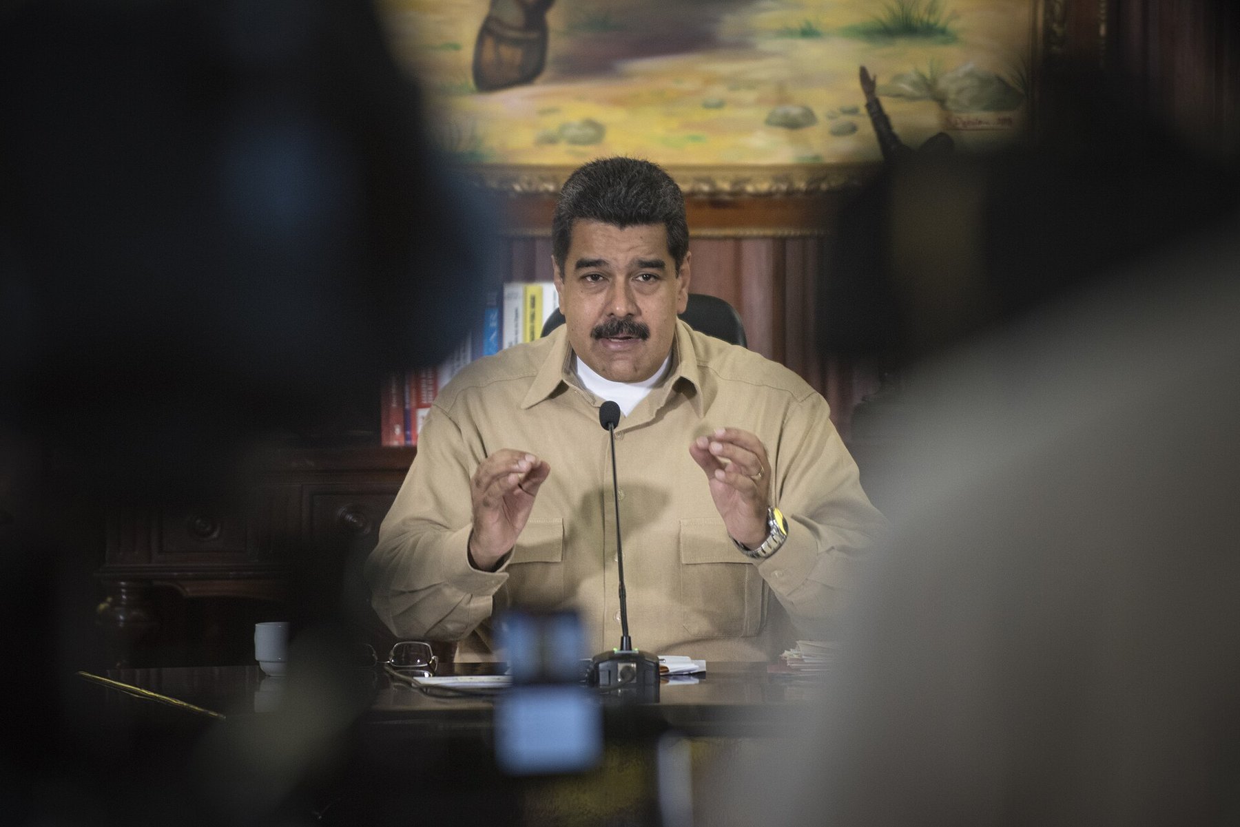 Nicolás Maduro speaking at a desk with a microphone during a December 2016 media appearance in Caracas