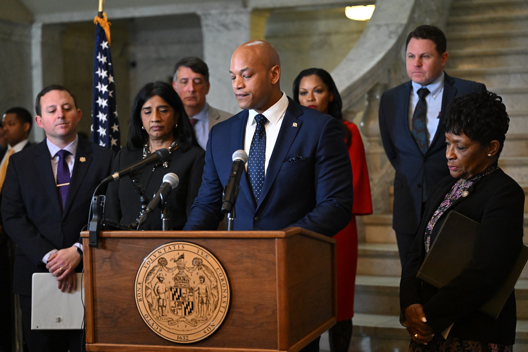 Gov. Wes Moore speaking at a podium bearing the Maryland state seal inside the Maryland State House, flanked by the General Assembly's presiding officers