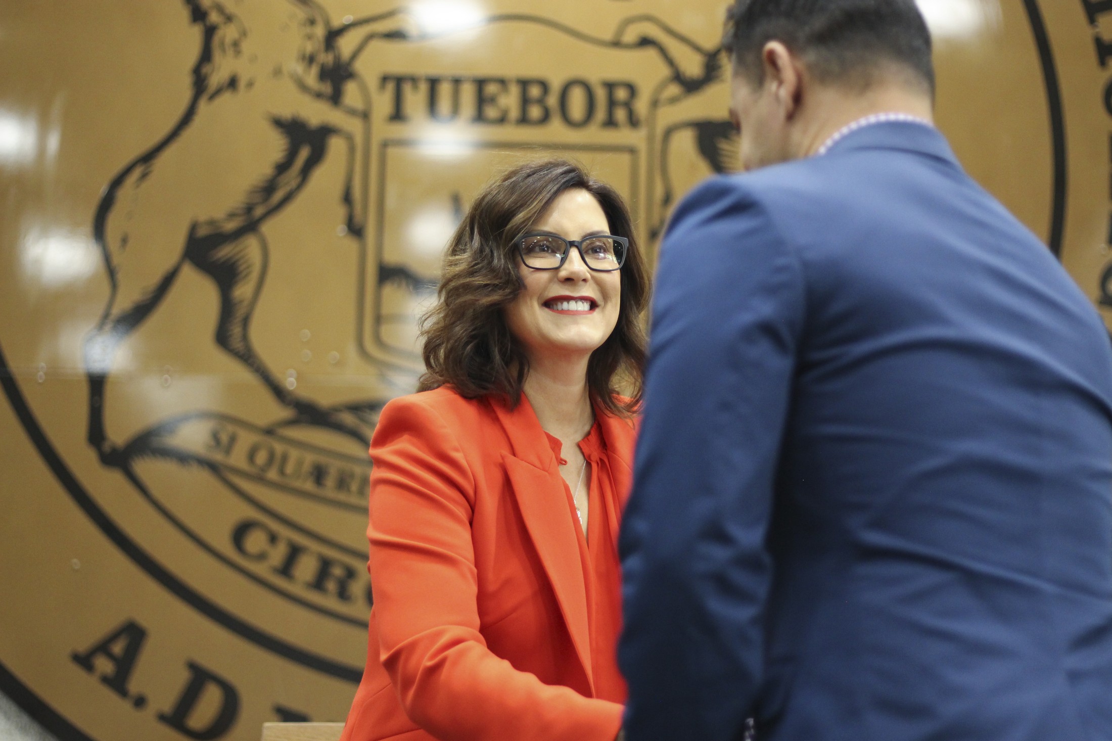 Michigan Gov. Gretchen Whitmer speaking with a colleague in front of the state seal
