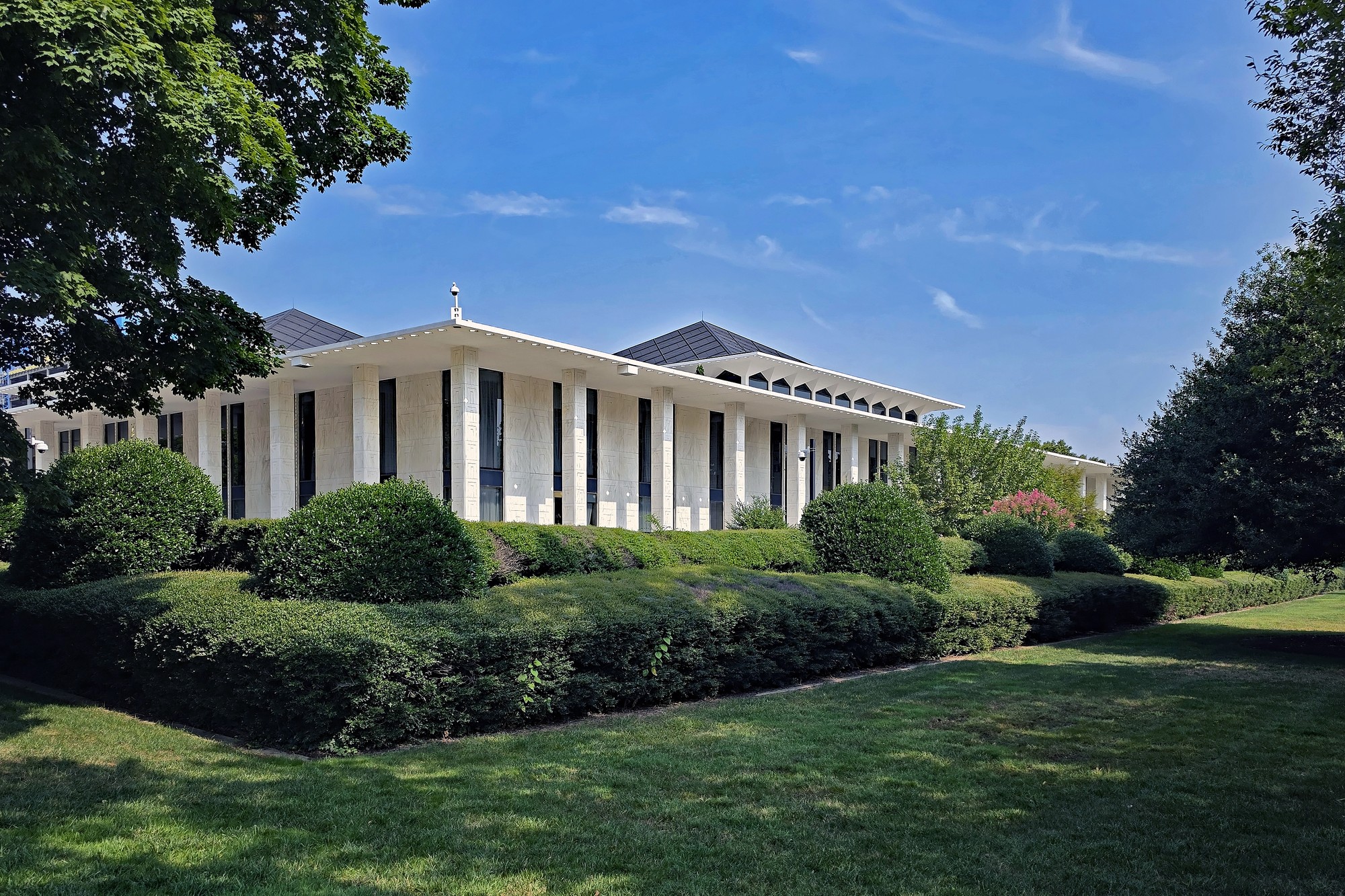 The North Carolina State Legislative Building in Raleigh, a low white marble structure with a colonnade and pyramidal roof, seen across its lawn and hedges