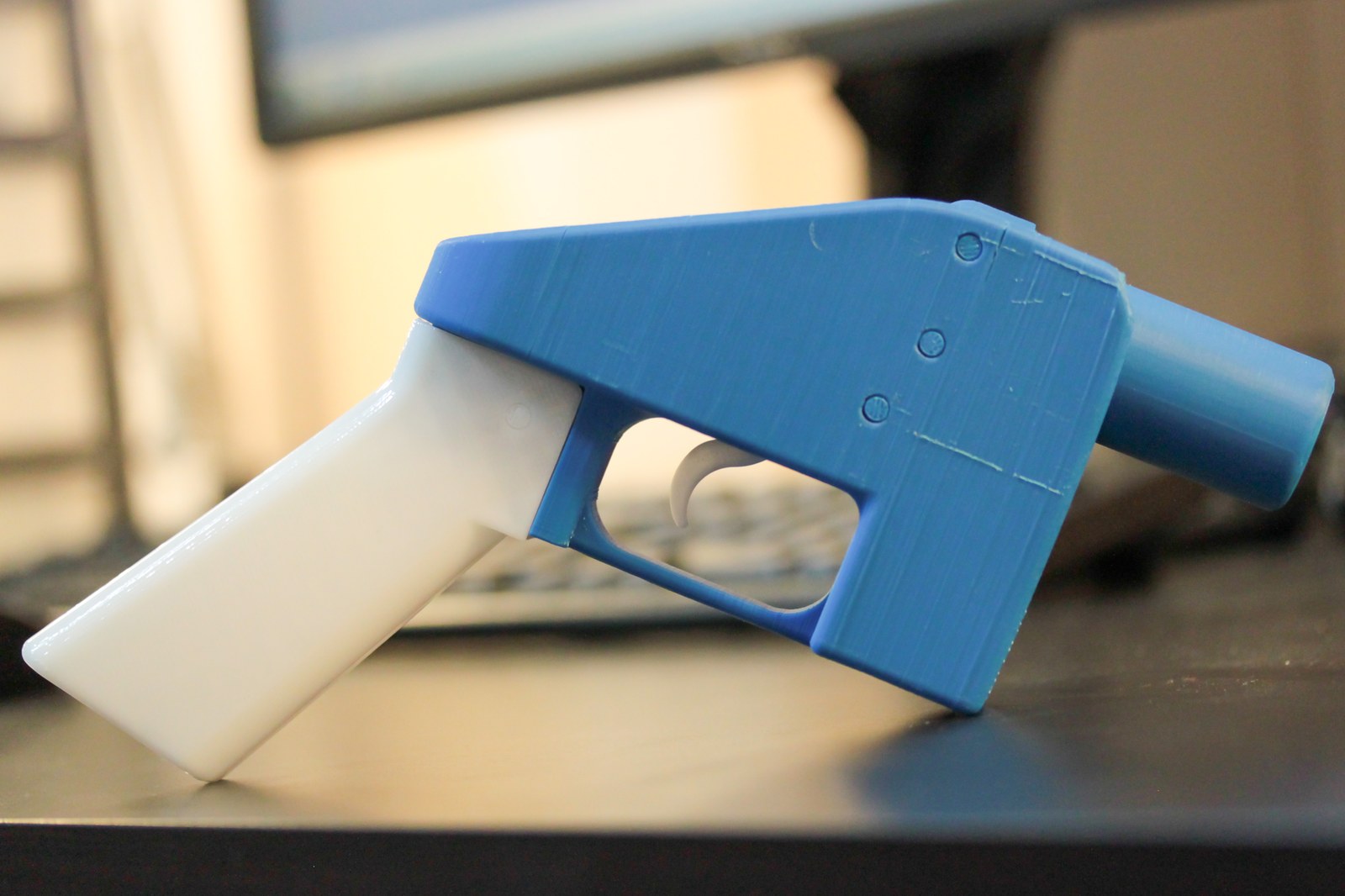 The Liberator, a single-shot pistol 3D printed in blue and white plastic, sitting on a desk beside a keyboard
