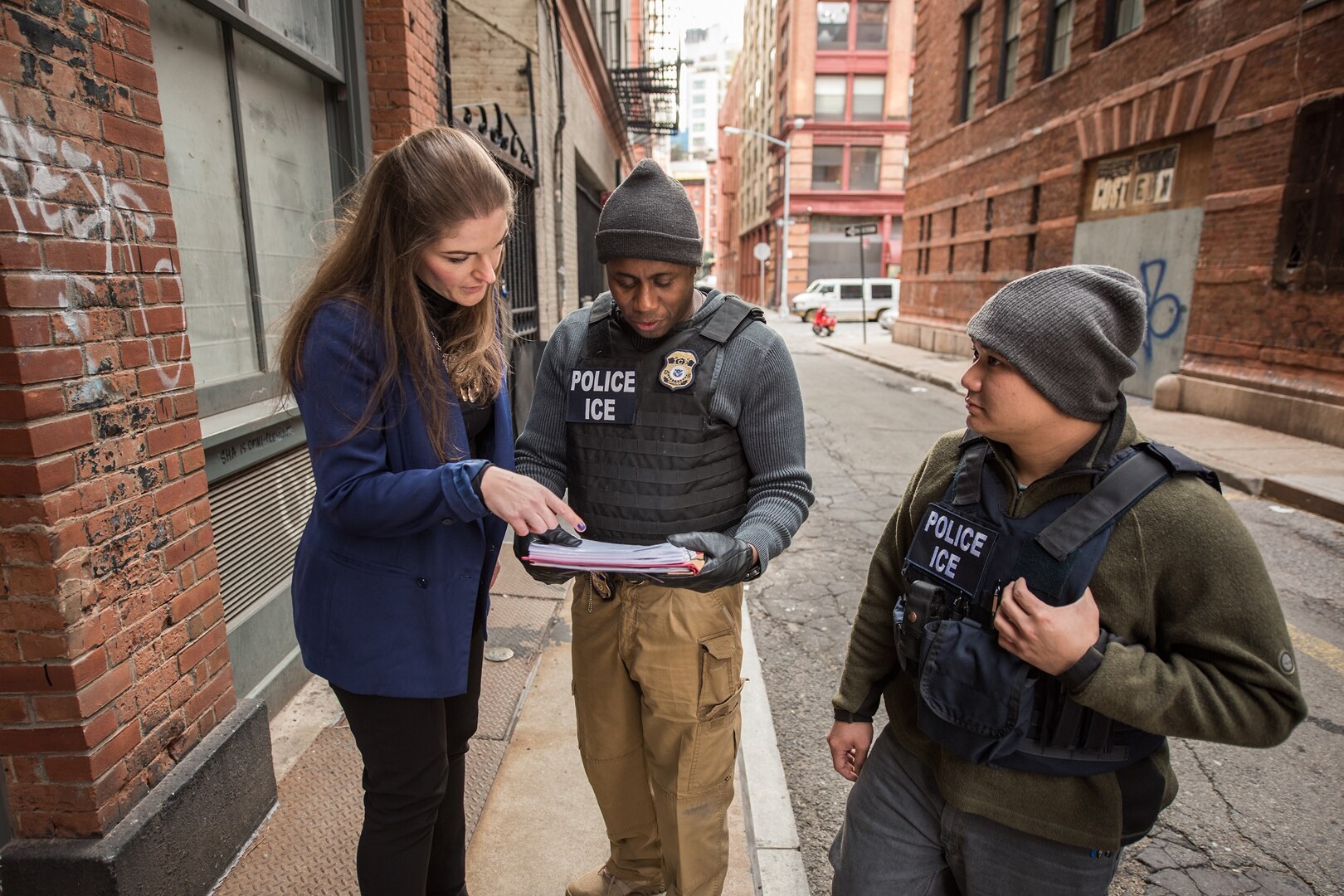 Two ICE officers and an attorney review paperwork on a New York City street
