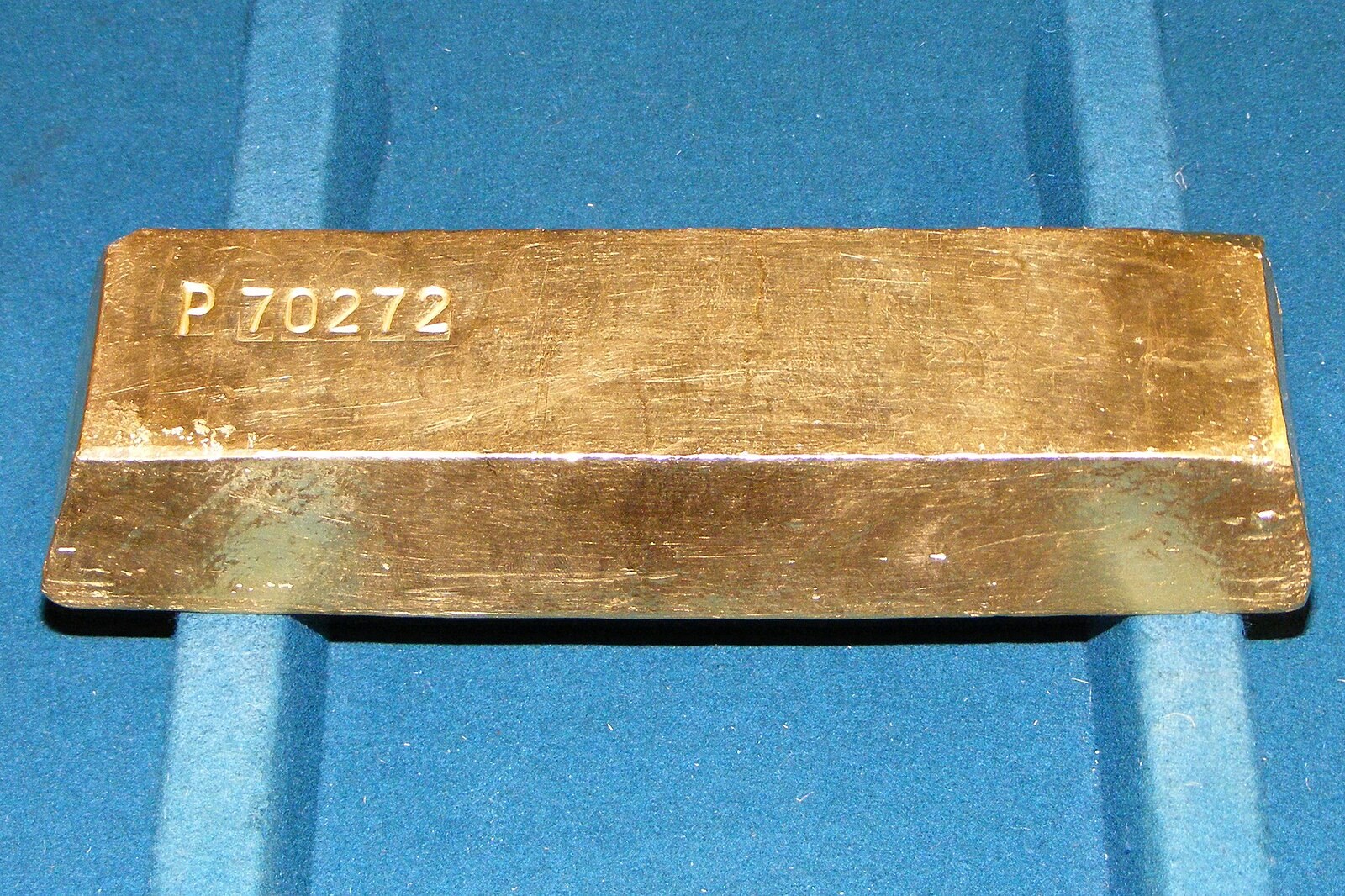 A 400 troy ounce gold bullion bar stamped with a serial number, resting on a blue cloth