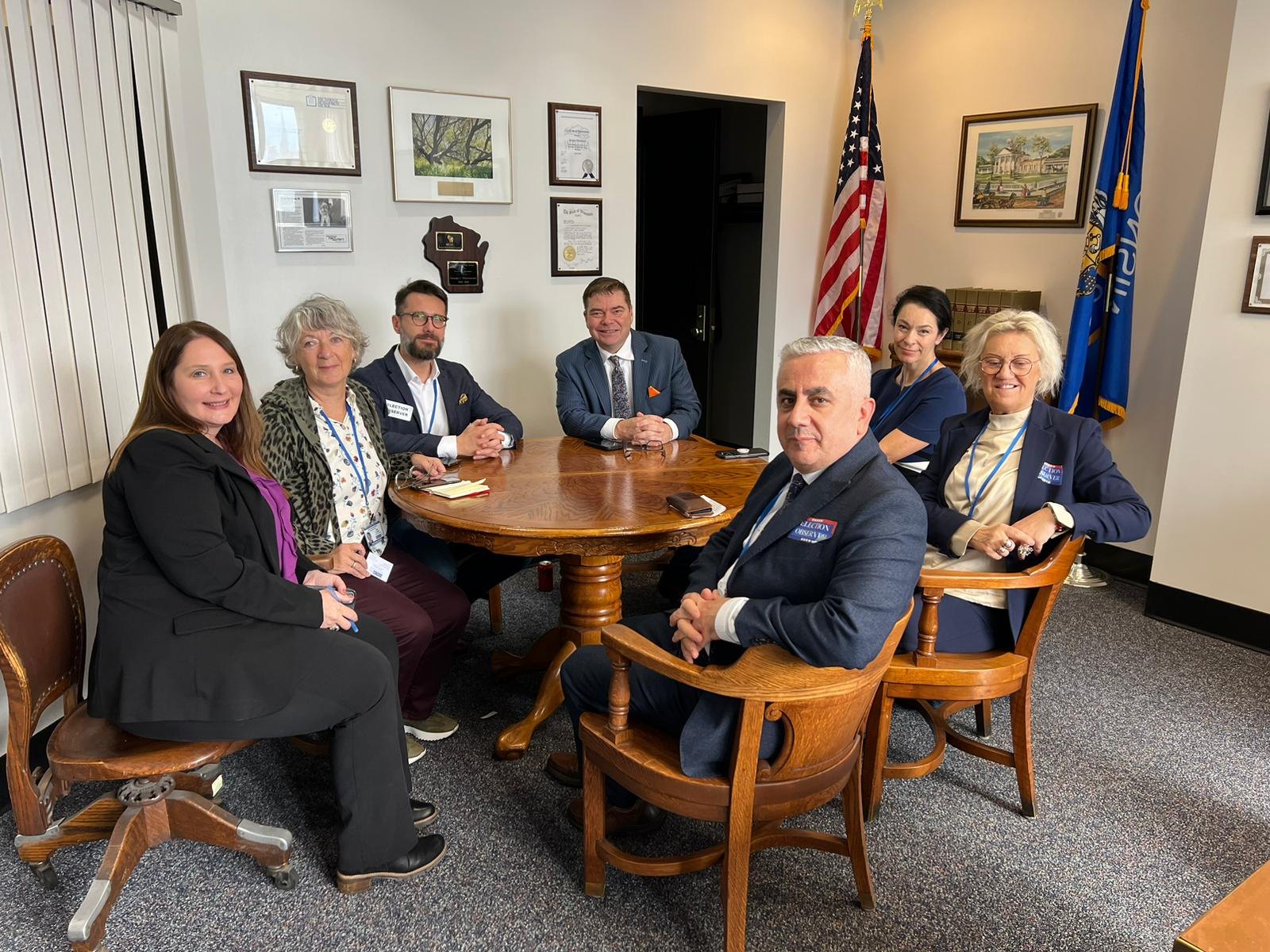 Members of an OSCE observer delegation seated around a table in a Wisconsin office during the 2024 U.S. election