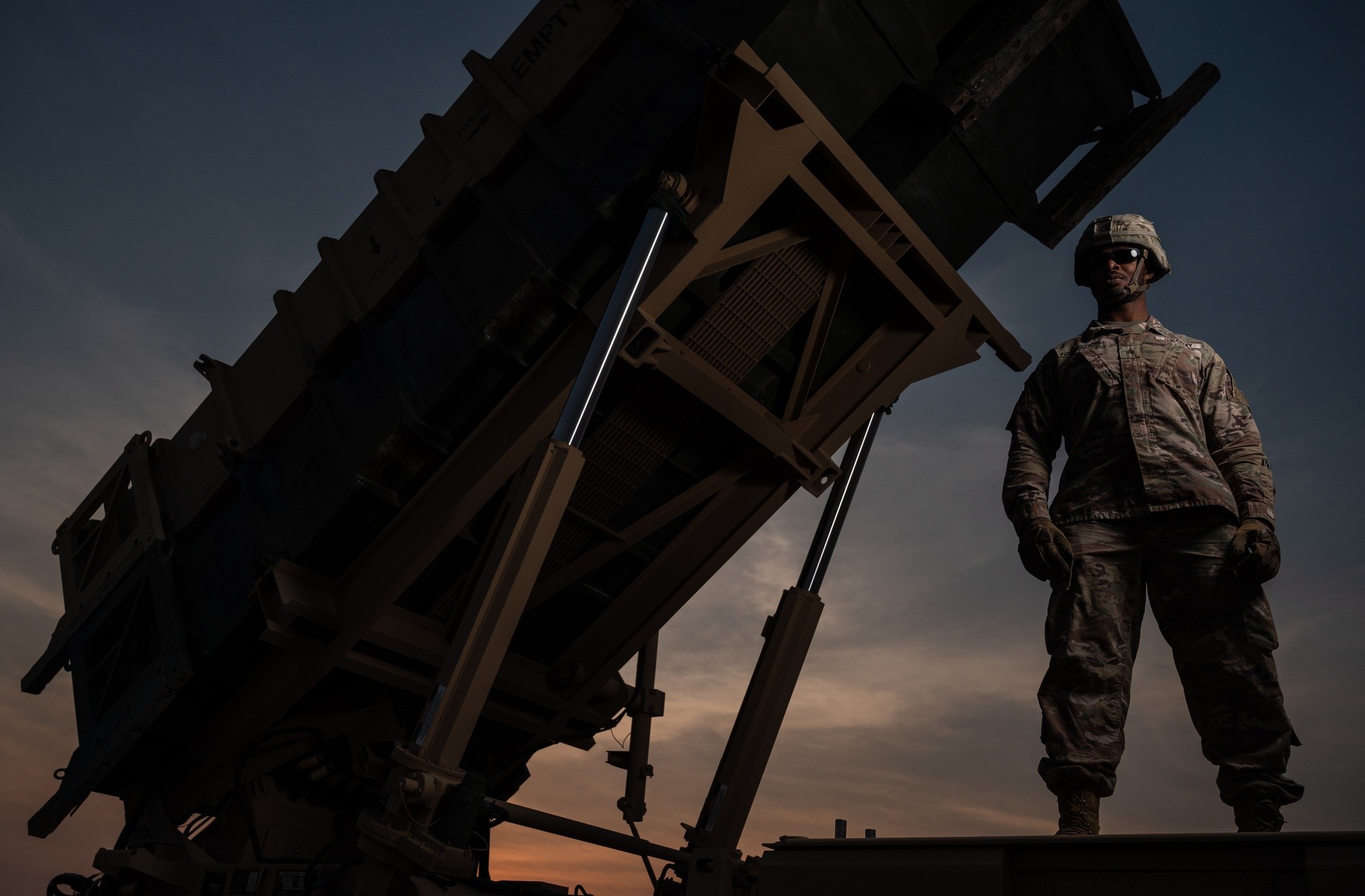 A U.S. Army Patriot battery operator stands beside a raised Patriot missile launcher at dusk at an undisclosed location in the U.S. Central Command area of responsibility