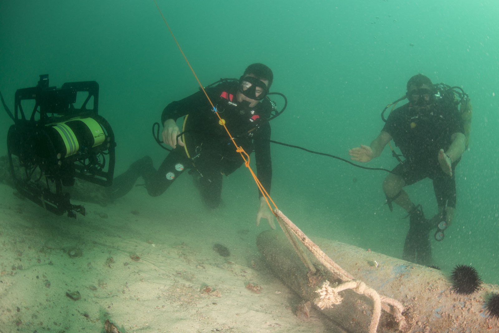Two military divers working alongside a remotely operated underwater vehicle on the seabed of the Arabian Gulf