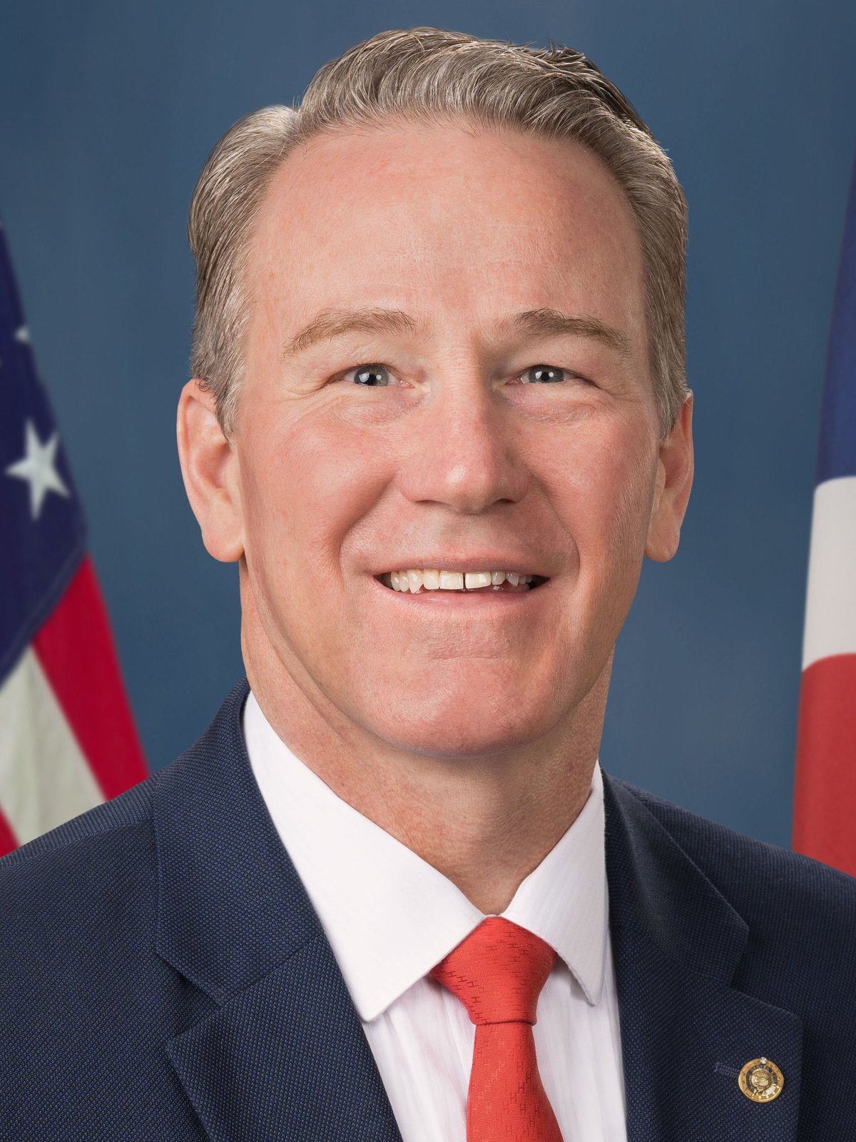 Official portrait of U.S. Senator Jon Husted of Ohio in front of American and Ohio flags