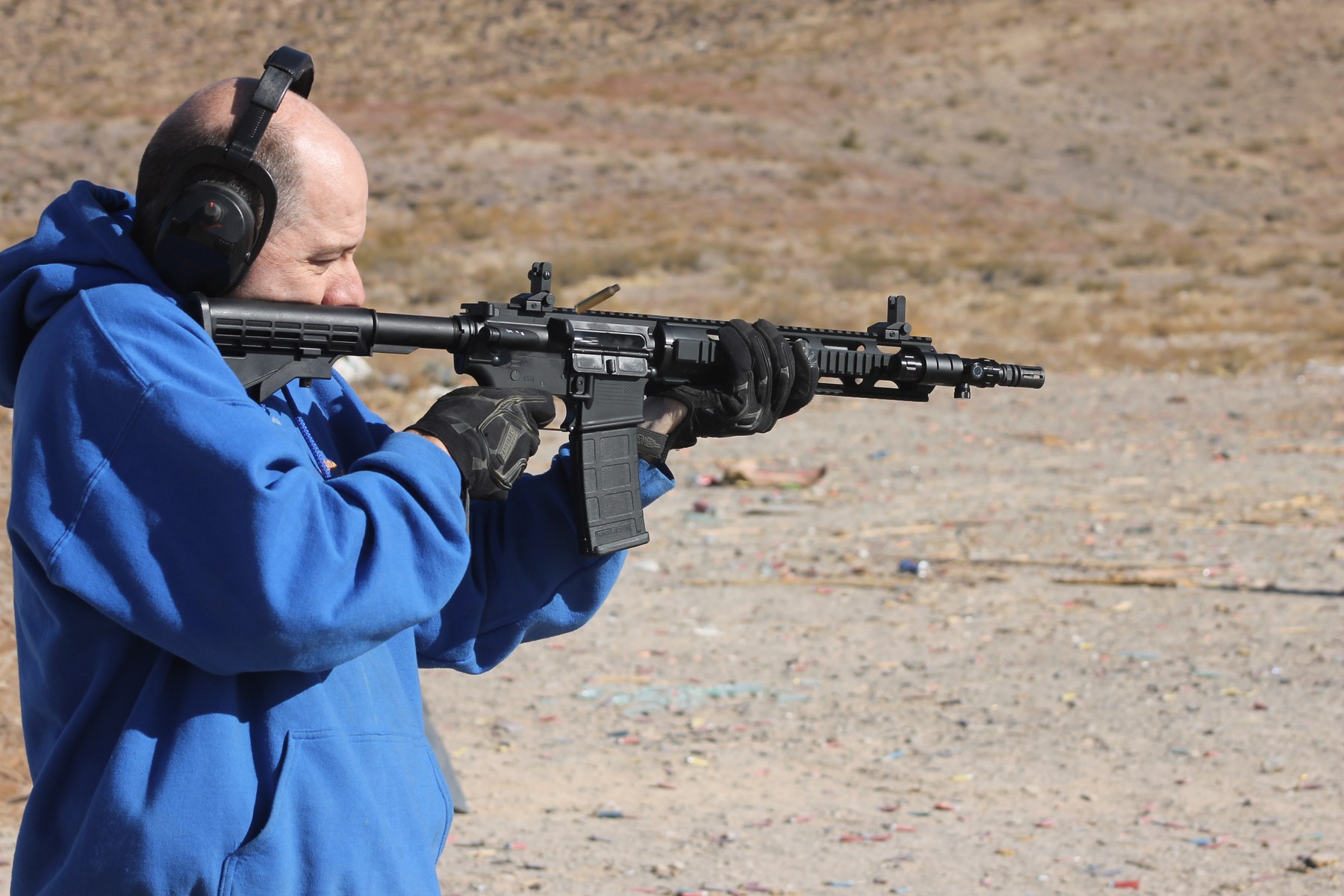 A man wearing hearing protection fires an AR-15-platform rifle at an outdoor shooting range in Nevada