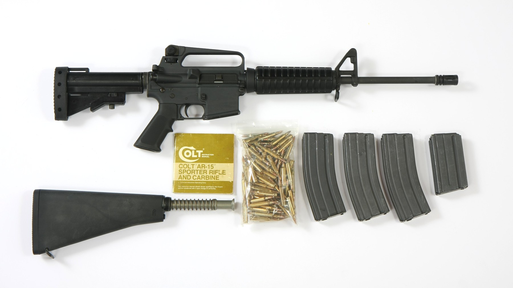 A pre-ban Colt AR-15 Sporter Lightweight rifle with telescoping stock, pistol grip and flash suppressor, shown with its original Colt manual, 5.56mm rounds and four magazines