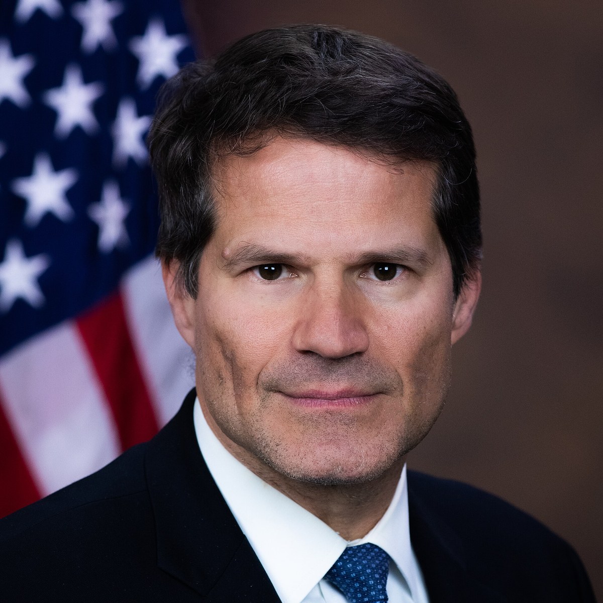Official portrait of Solicitor General D. John Sauer in a dark suit in front of an American flag
