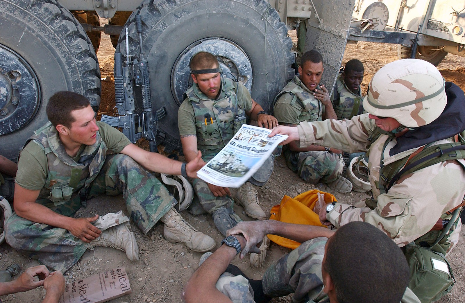 Command Sgt. Maj. John Sparks hands copies of Stars and Stripes to U.S. Marines sitting in the dirt beside a truck in Iraq in April 2003