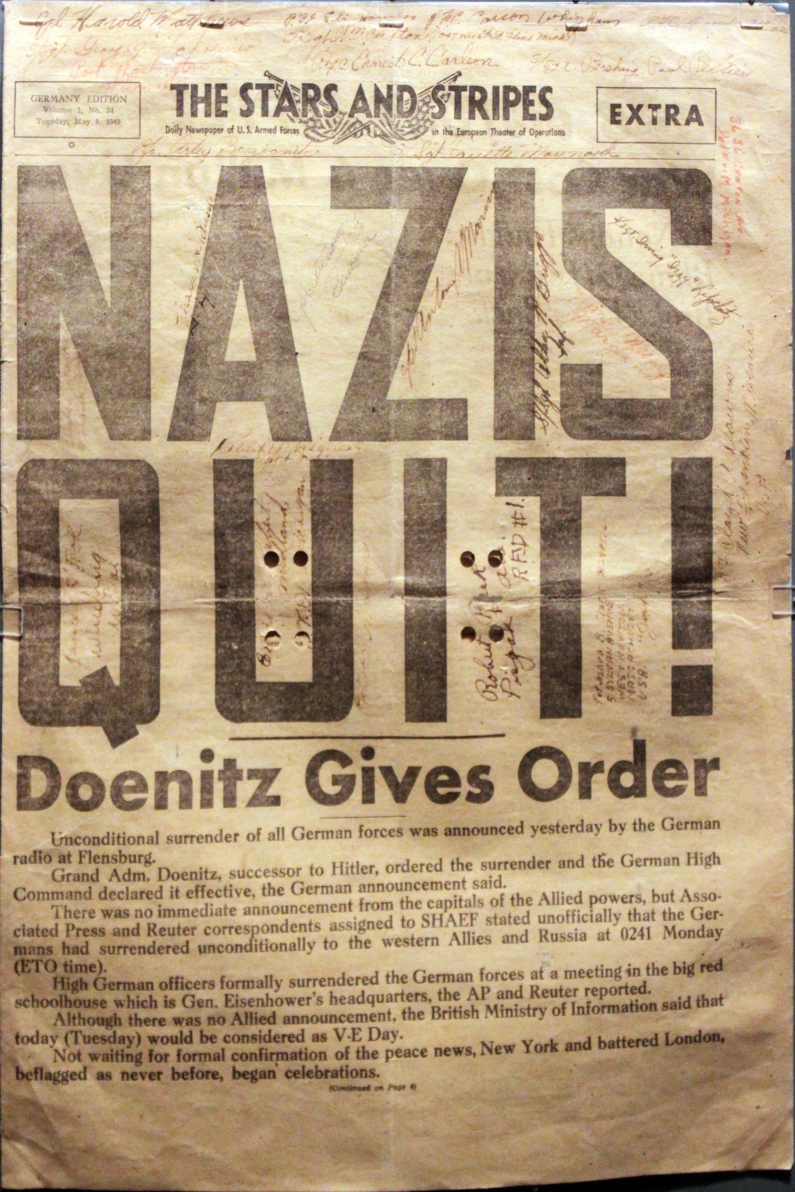 Front page of The Stars and Stripes Germany Edition Extra of May 8, 1945, with the headline NAZIS QUIT and the subhead Doenitz Gives Order, covered in handwritten soldiers' signatures