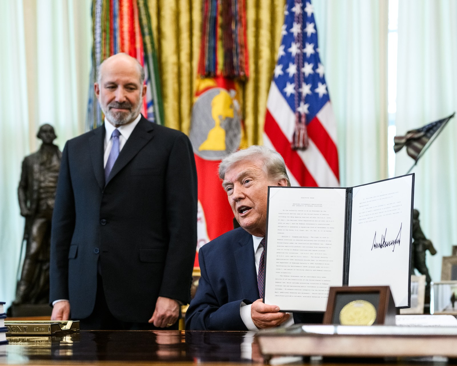 President Donald Trump holds up the signed executive order limiting mail-in voting in the Oval Office on March 31, 2026
