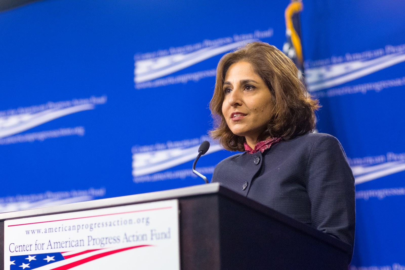Neera Tanden speaking at a lectern marked Center for American Progress Action Fund in front of a blue Center for American Progress backdrop
