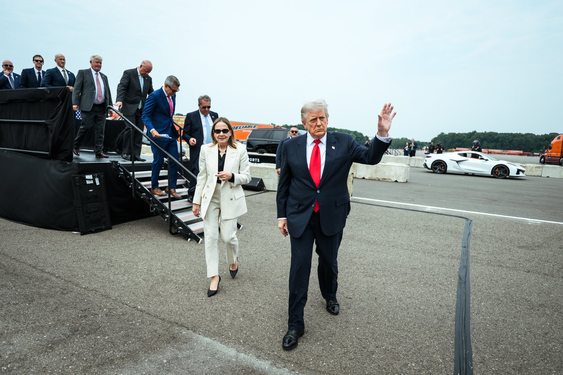 President Donald Trump waves as he walks beside GM CEO Mary Barra on the test track at the General Motors Proving Ground in Milford, Michigan, with a white Corvette behind them