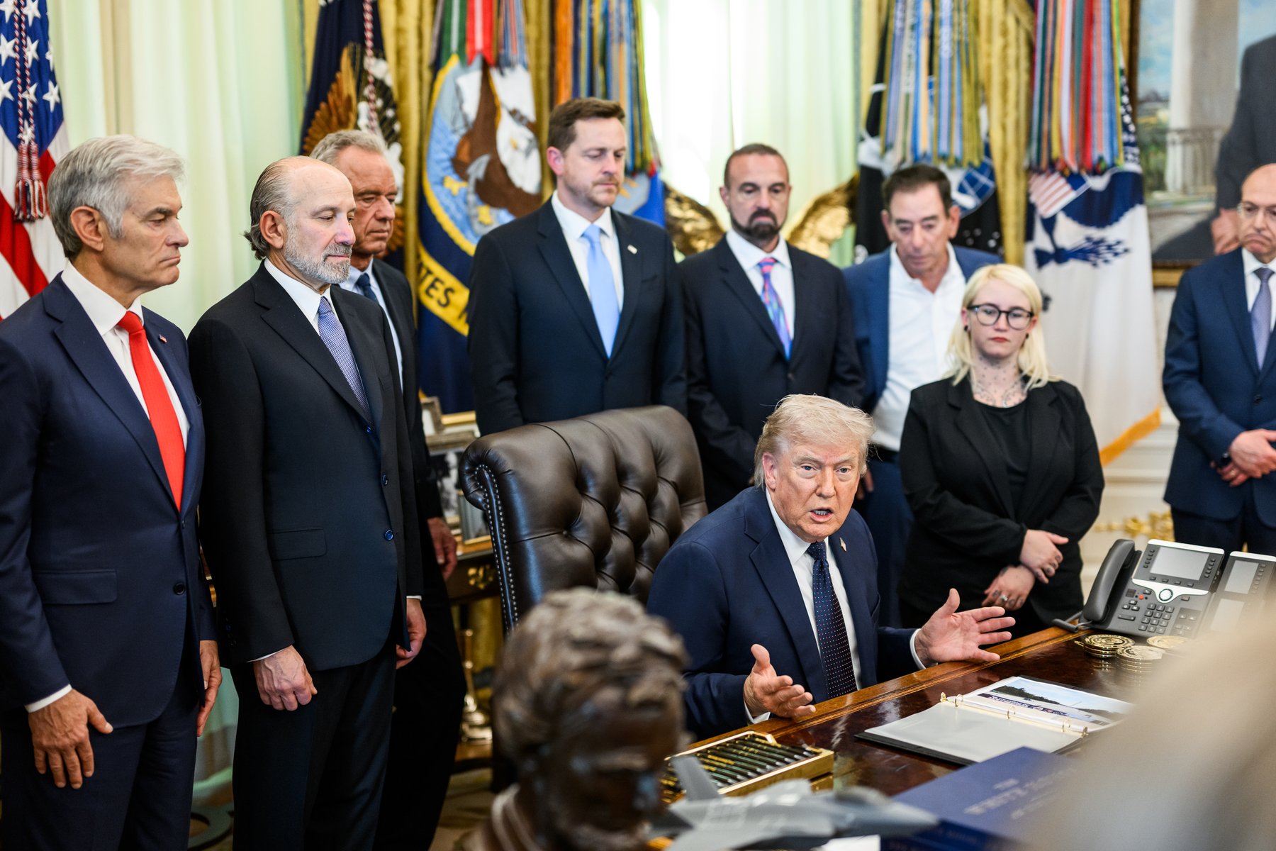 President Donald Trump seated at the Resolute Desk during an April 2026 health care affordability event in the Oval Office, with administration health officials standing behind him