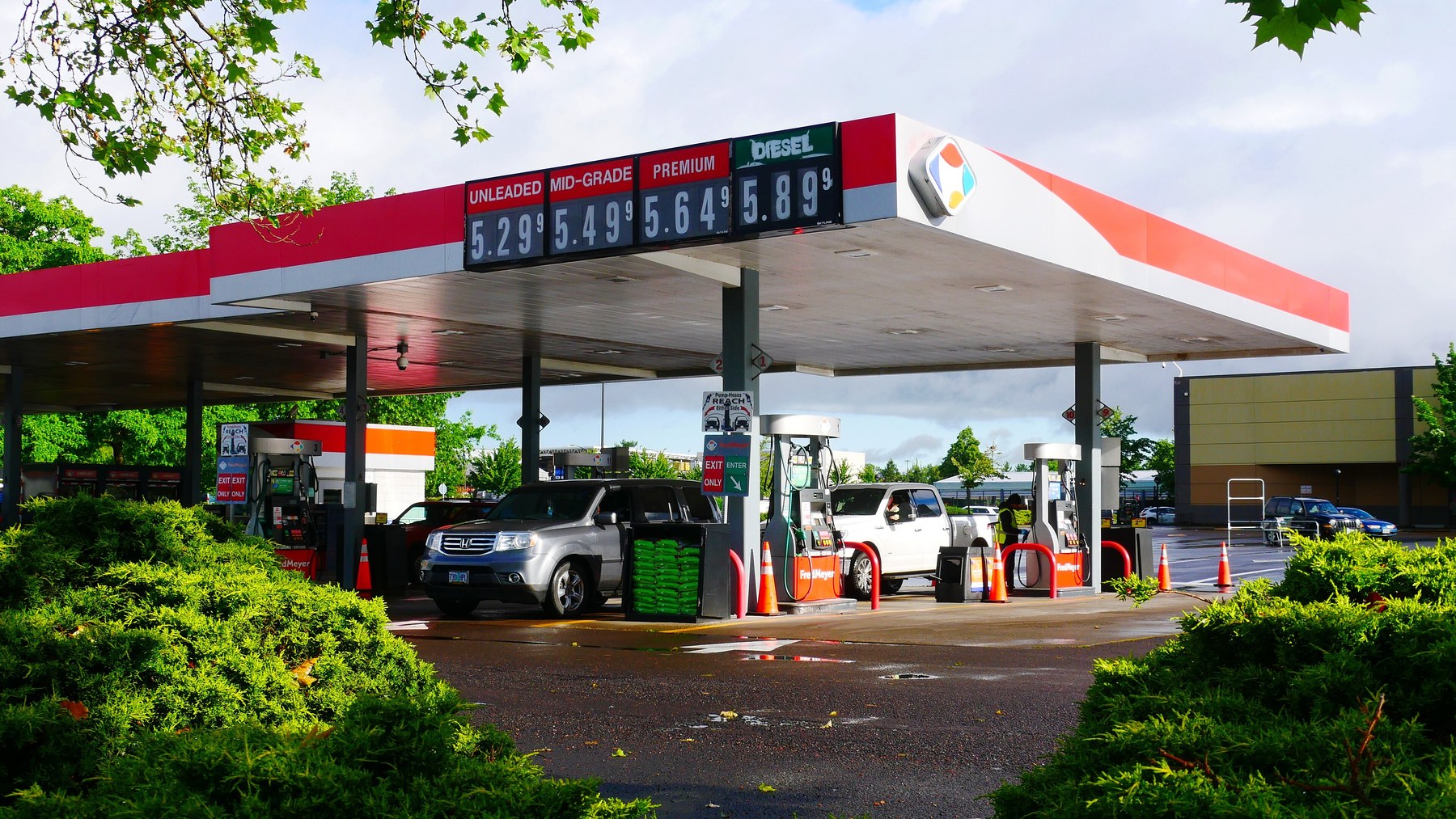 Gas station canopy with posted prices of 5.29 for unleaded and 5.89 for diesel, with two vehicles at the pumps