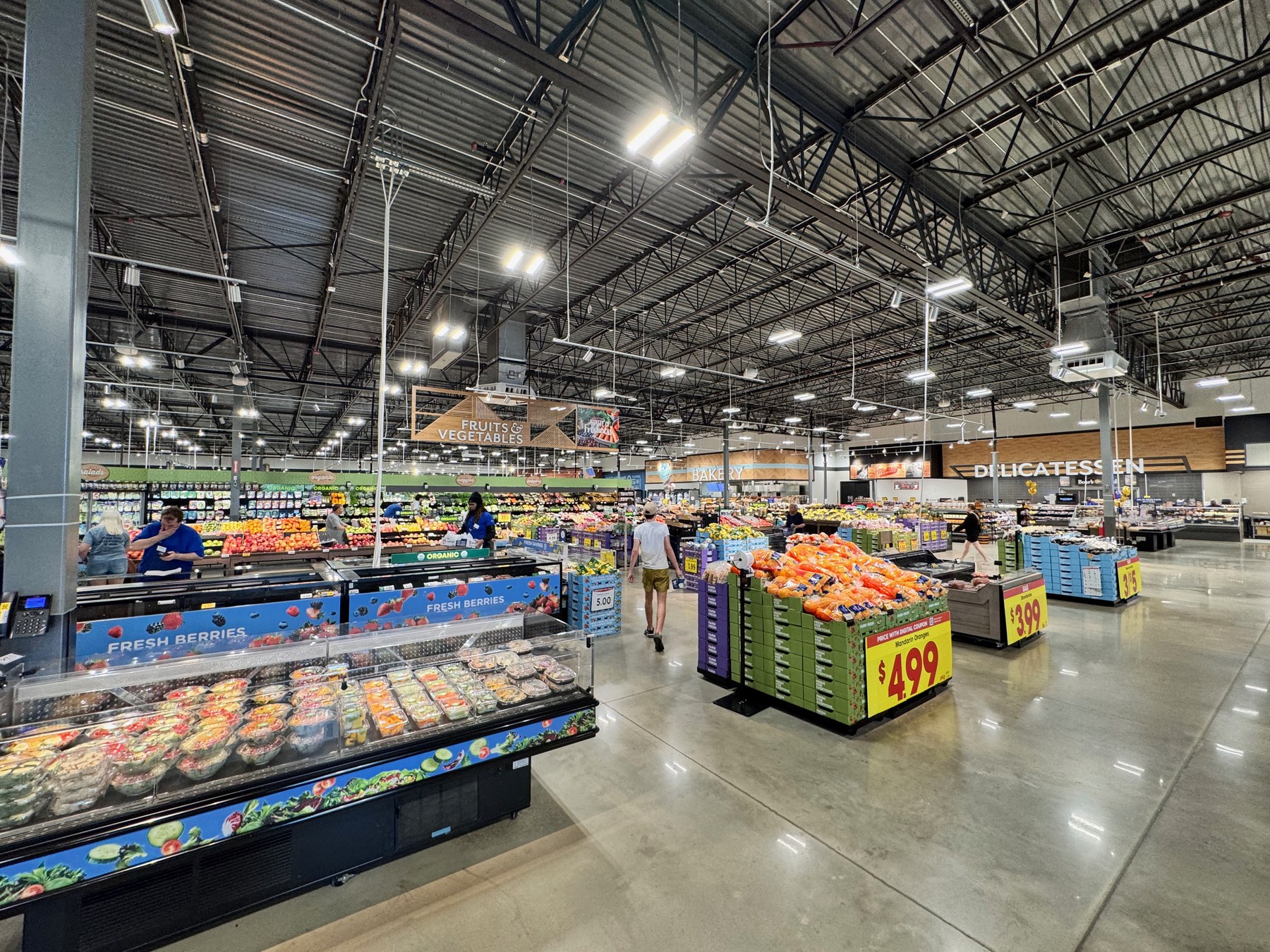 The produce and fresh food section of a large Kroger Marketplace supermarket, with shoppers and a promotional price sign visible