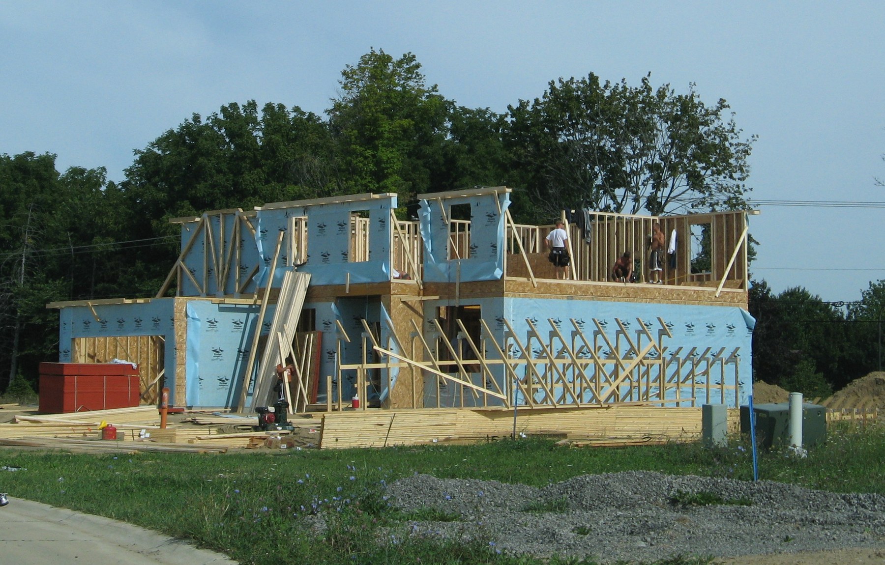 A new single-family house under construction with framing and exterior sheathing visible, workers on the second floor