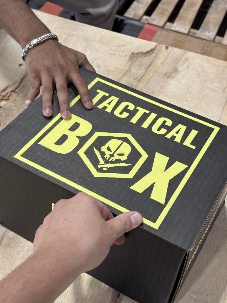 Hands sealing a TacticalBox shipment on the packing bench — the next Welcome Box going out