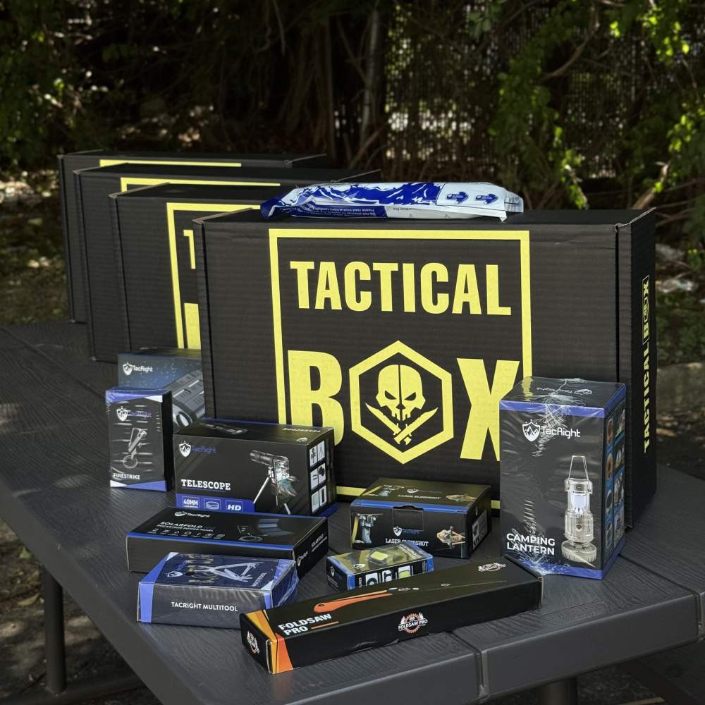 Several TacticalBox shipments on an outdoor table with TacRight gear unpacked beside them — telescope, firestrike, lantern, foldsaw