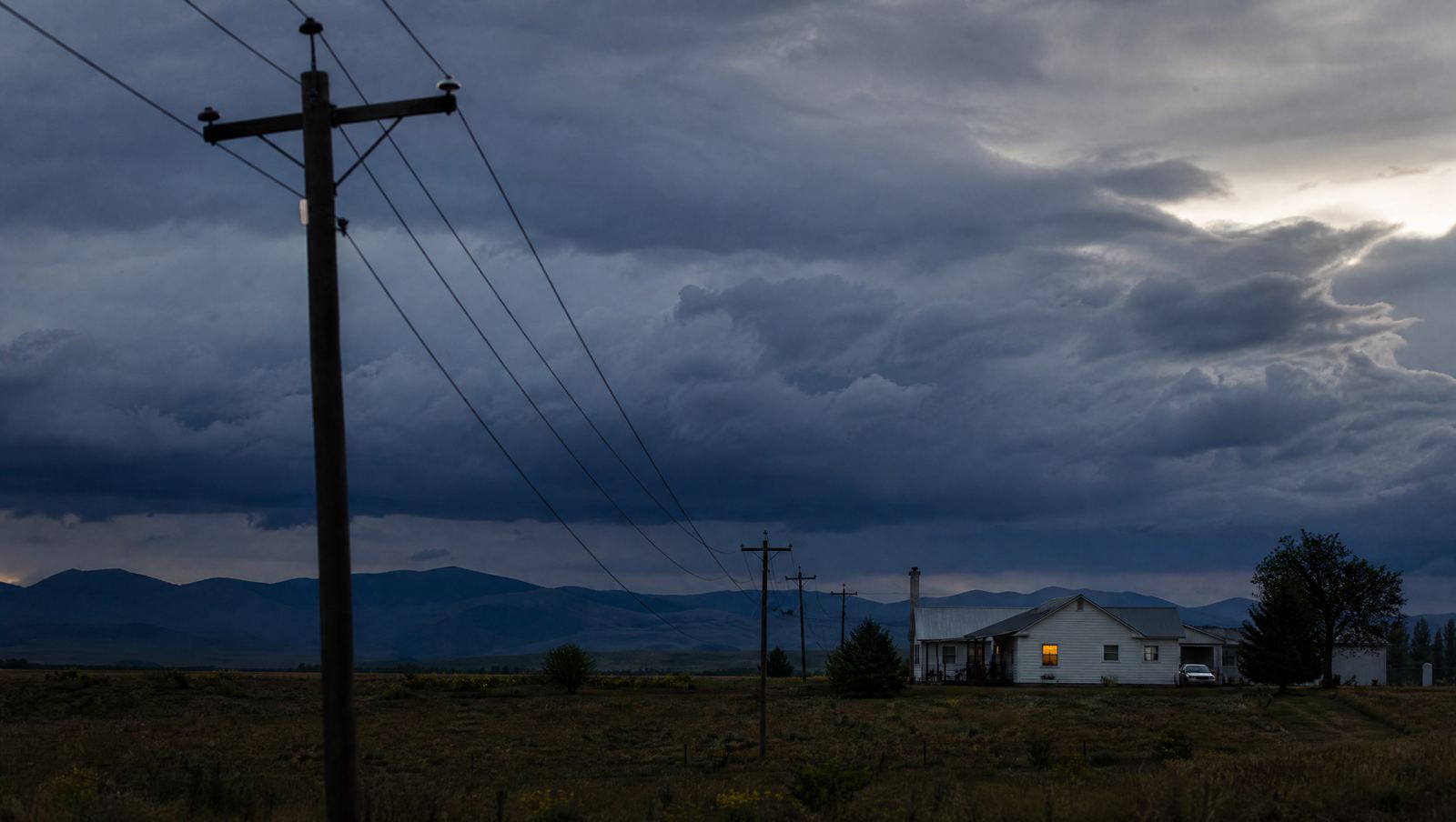 Storm clouds gathering over power lines and a rural home at dusk